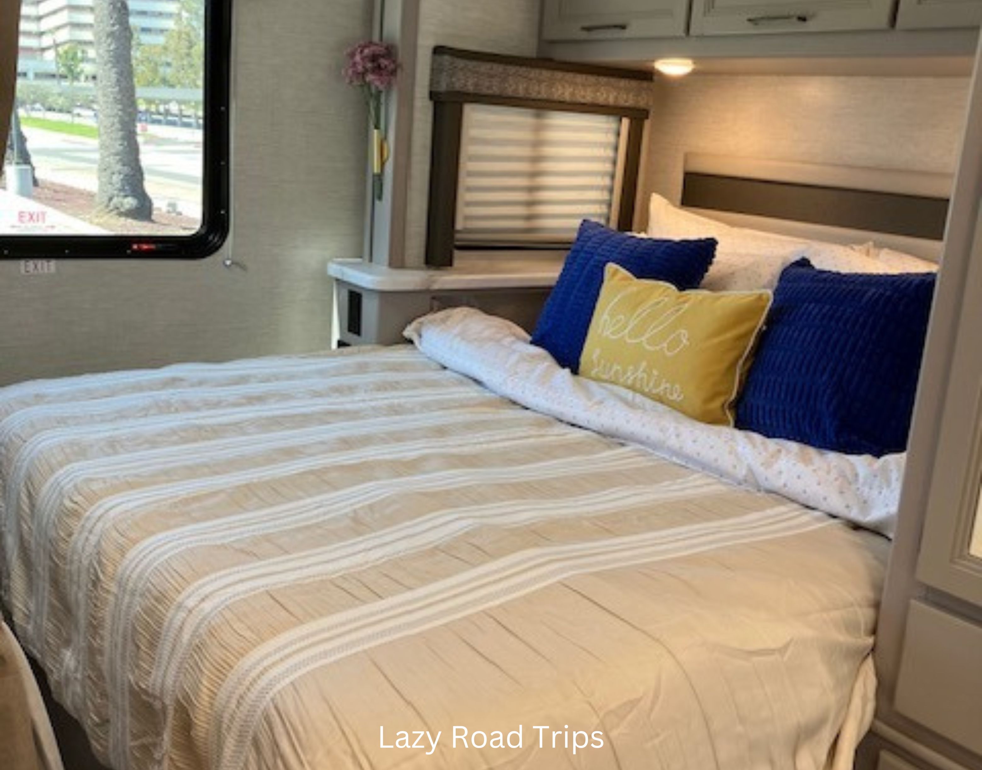 Cozy RV rental bedroom with a bed featuring light-striped bedding, blue, and a yellow "hello sunshine" pillow.. Thor Chateau 2024