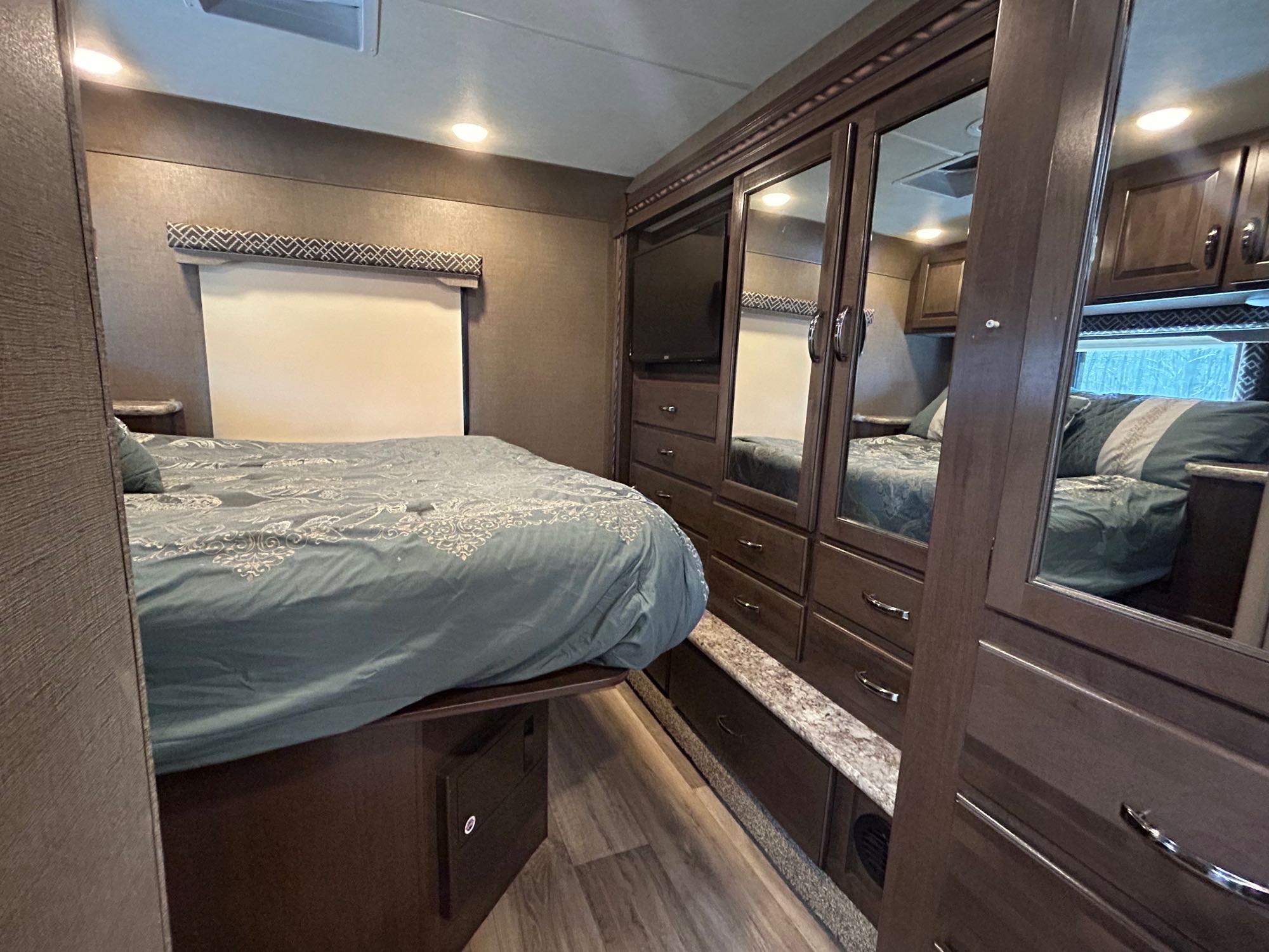 Inside a cozy RV rental bedroom: teal bed, mirrored wardrobe, TV, and ample storage for travel.. Thor Four Winds 2017