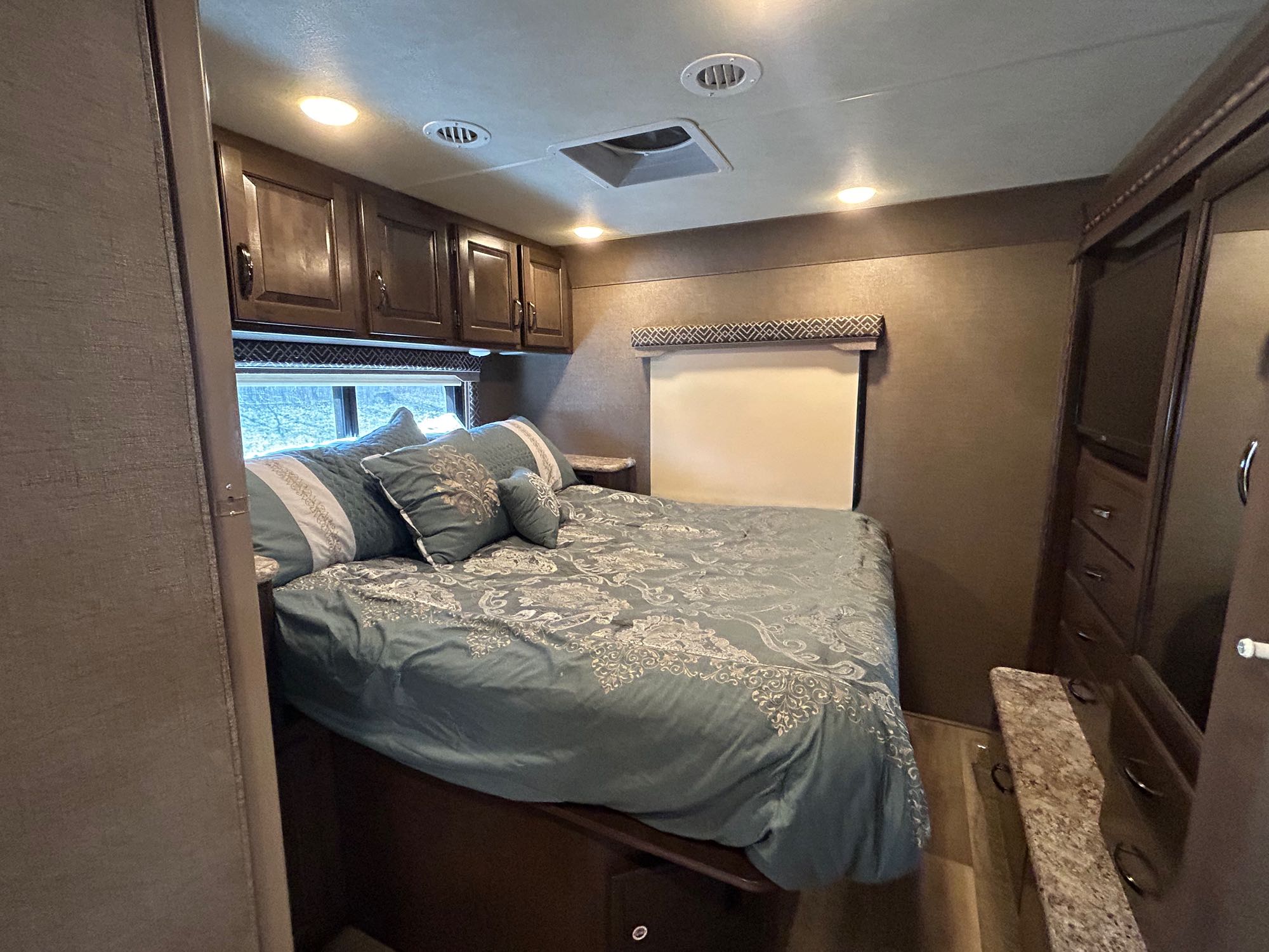 Cozy RV rental bedroom featuring a patterned bed, overhead cabinets, and built-in TV for comfortable travel.. Thor Four Winds 2017