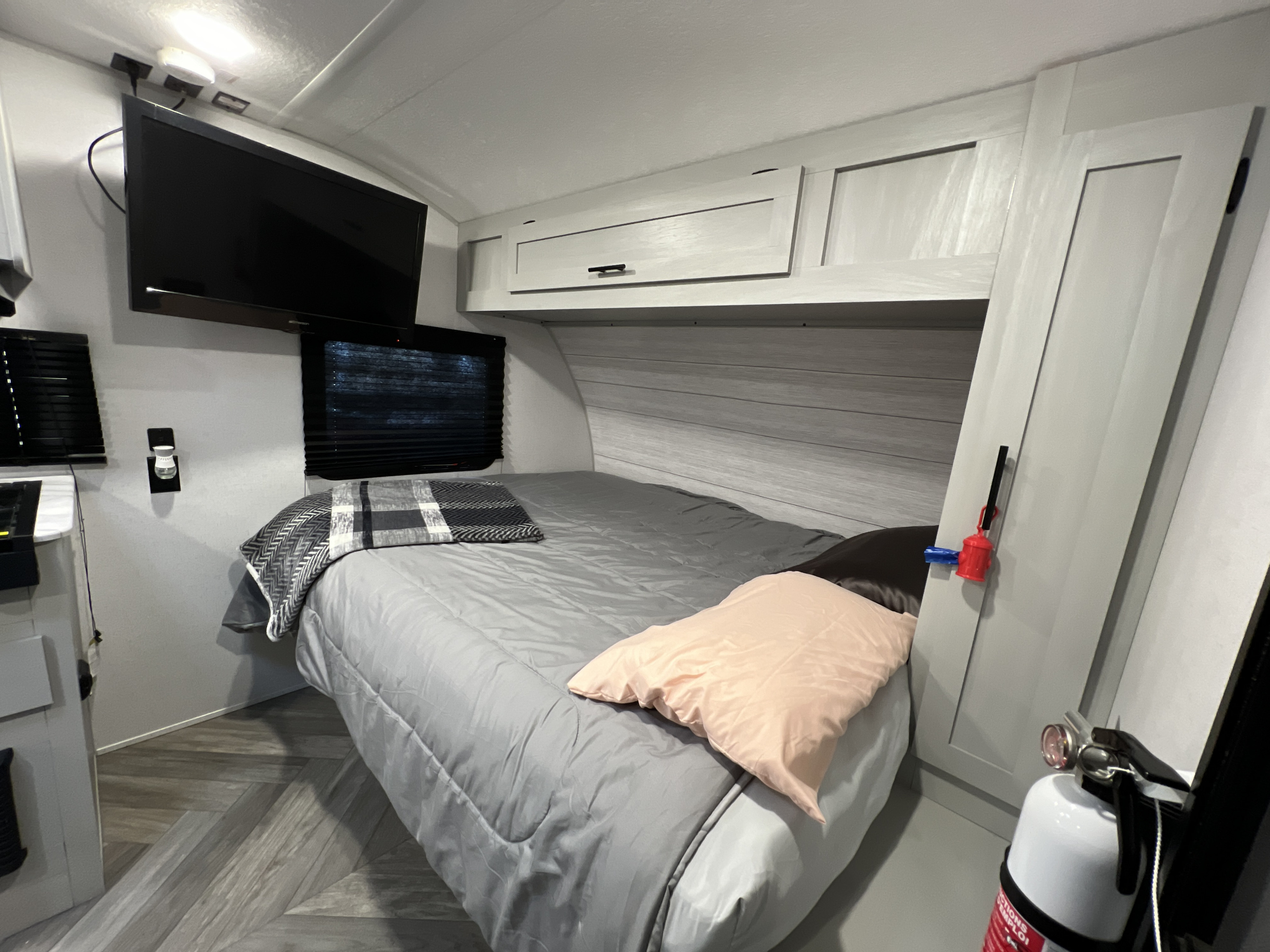 RV rental sleeping area featuring a queen-sized bed, wall-mounted TV, overhead cabinets, and a fire extinguisher.. Forest River Wildwood 2022