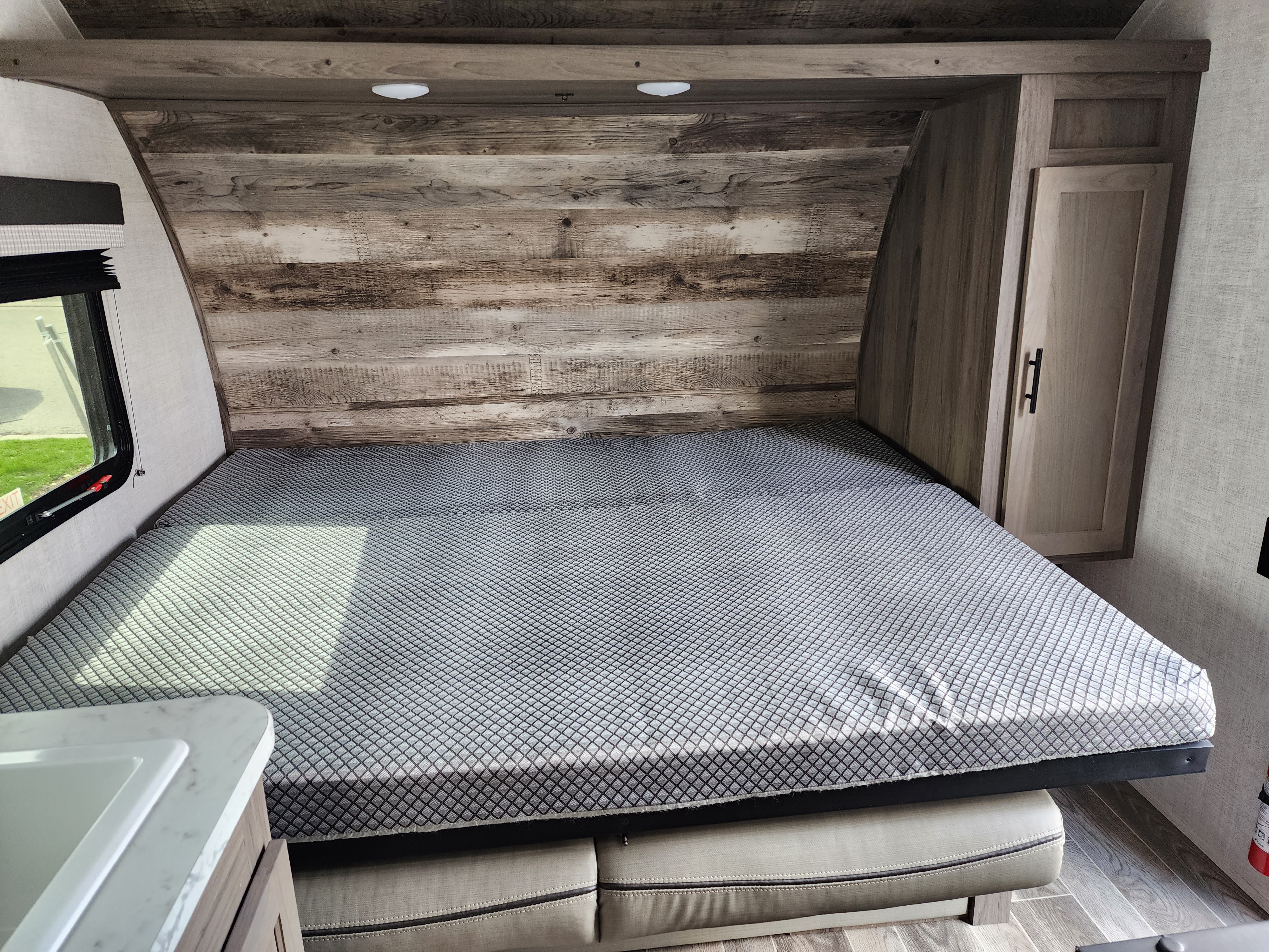 RV rental interior: A bed with a grey patterned cover, wood headboard, and side cabinet. Compact and functional space.. Gulf Stream 22MD 2022