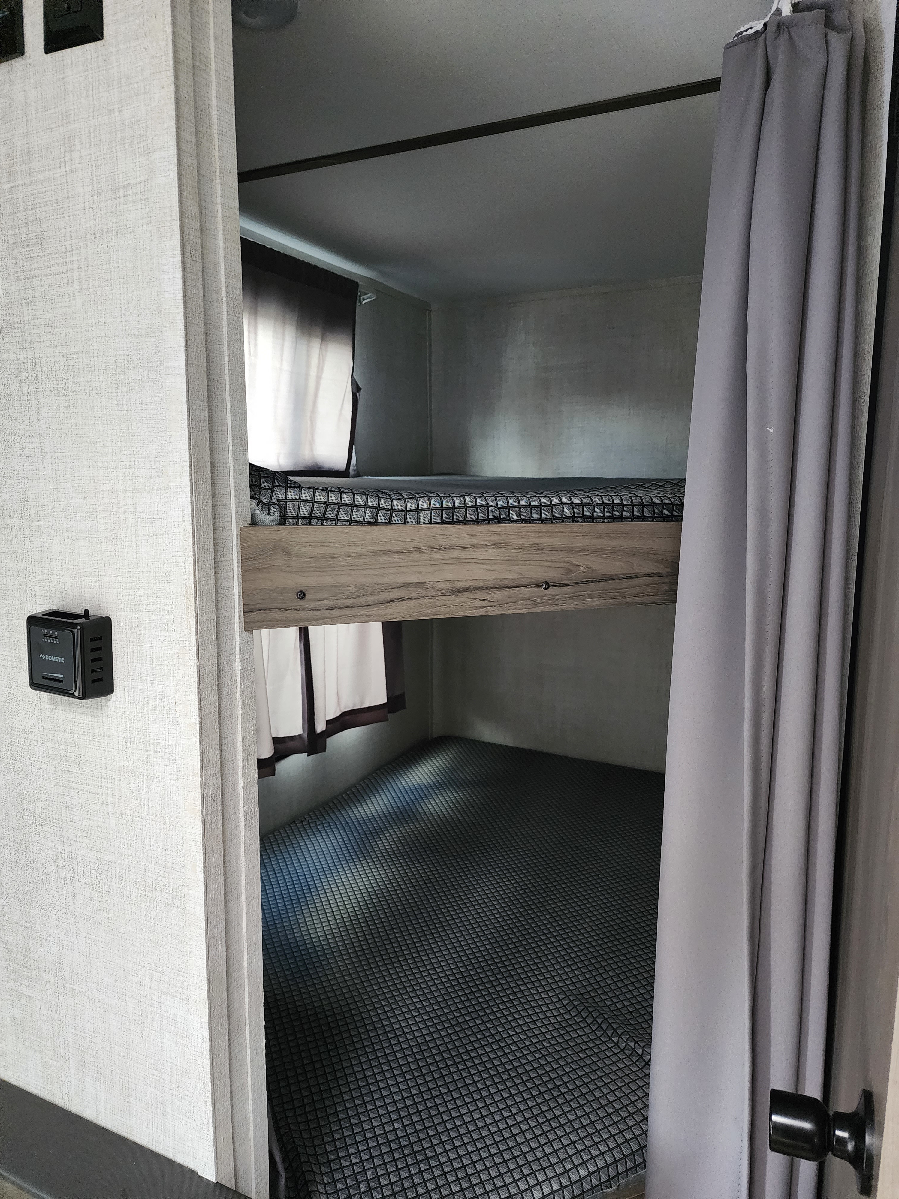 RV rental interior showing comfortable bunk beds with patterned covers and privacy curtains. A Dometic control panel is on the left wall.. Gulf Stream 22MD 2022