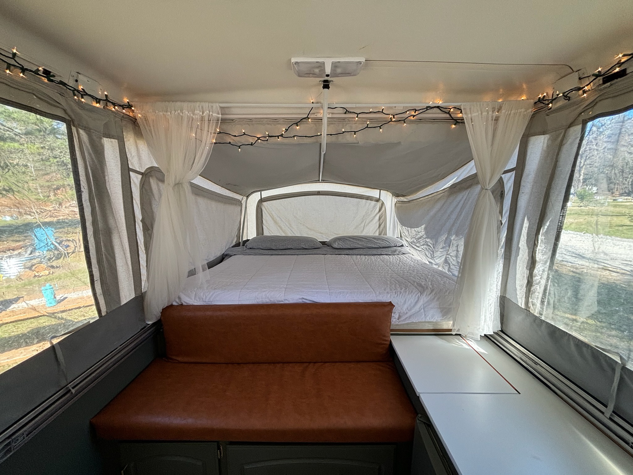 This inviting RV rental pop-up camper offers a large bed, comfy bench, and decorative string lights for a cozy stay.. Coleman Grand Tour Elite 2000