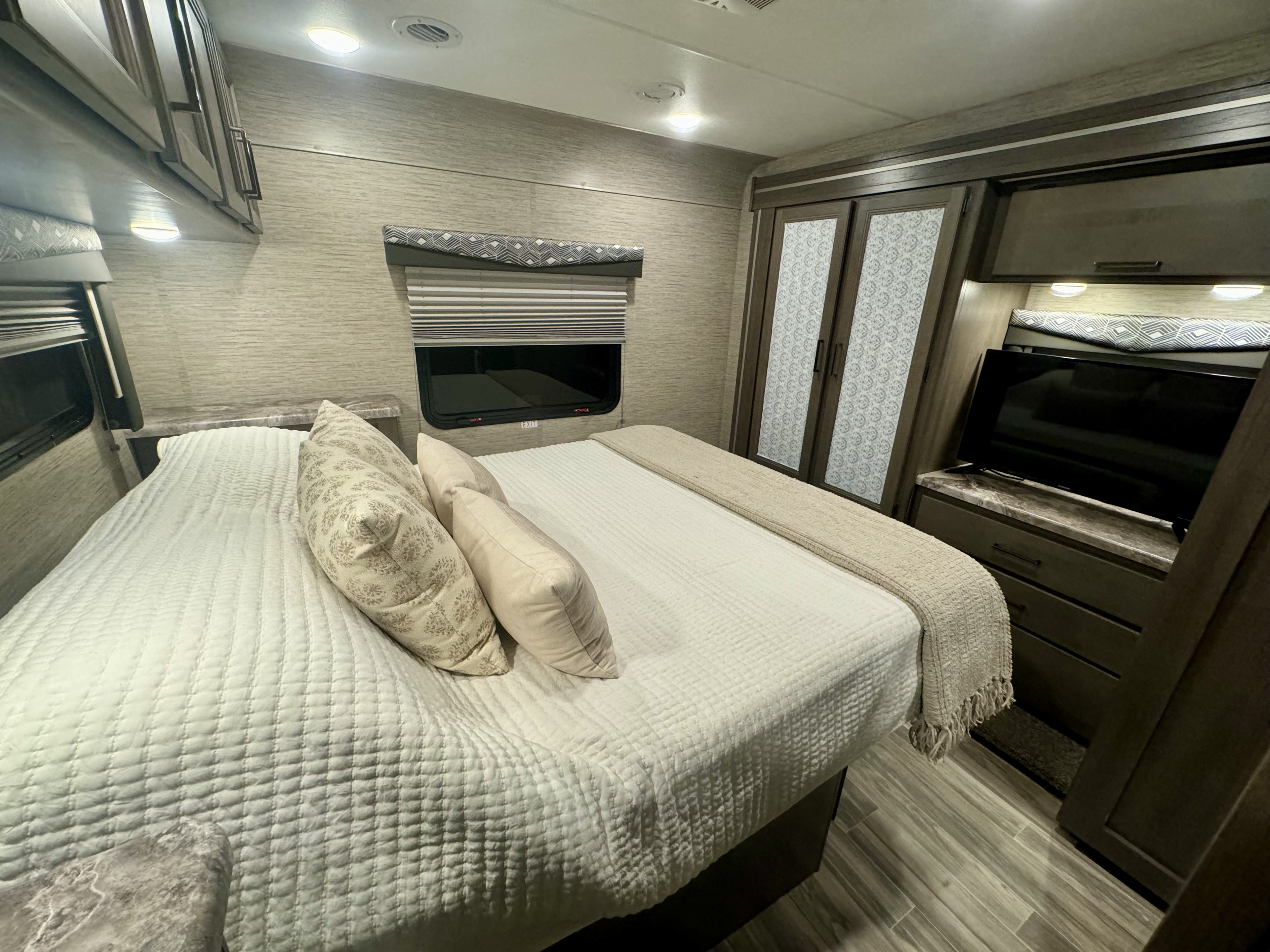 Spacious RV rental bedroom with a large bed, built-in storage, and TV, perfect for comfortable travel.. thor four winds 2024