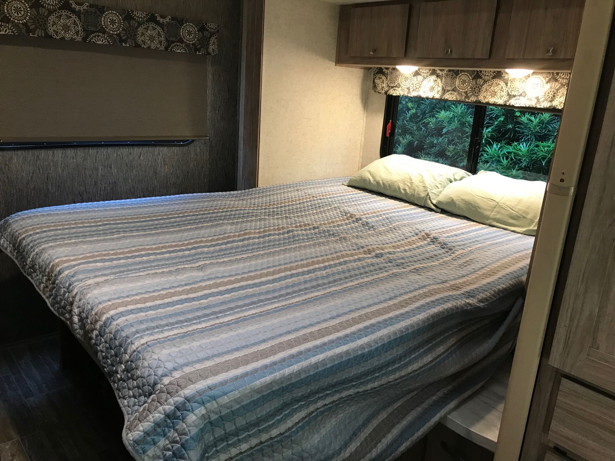 Cozy RV rental bedroom with striped bed, overhead storage, and nature views outside.. Forester LE 2018