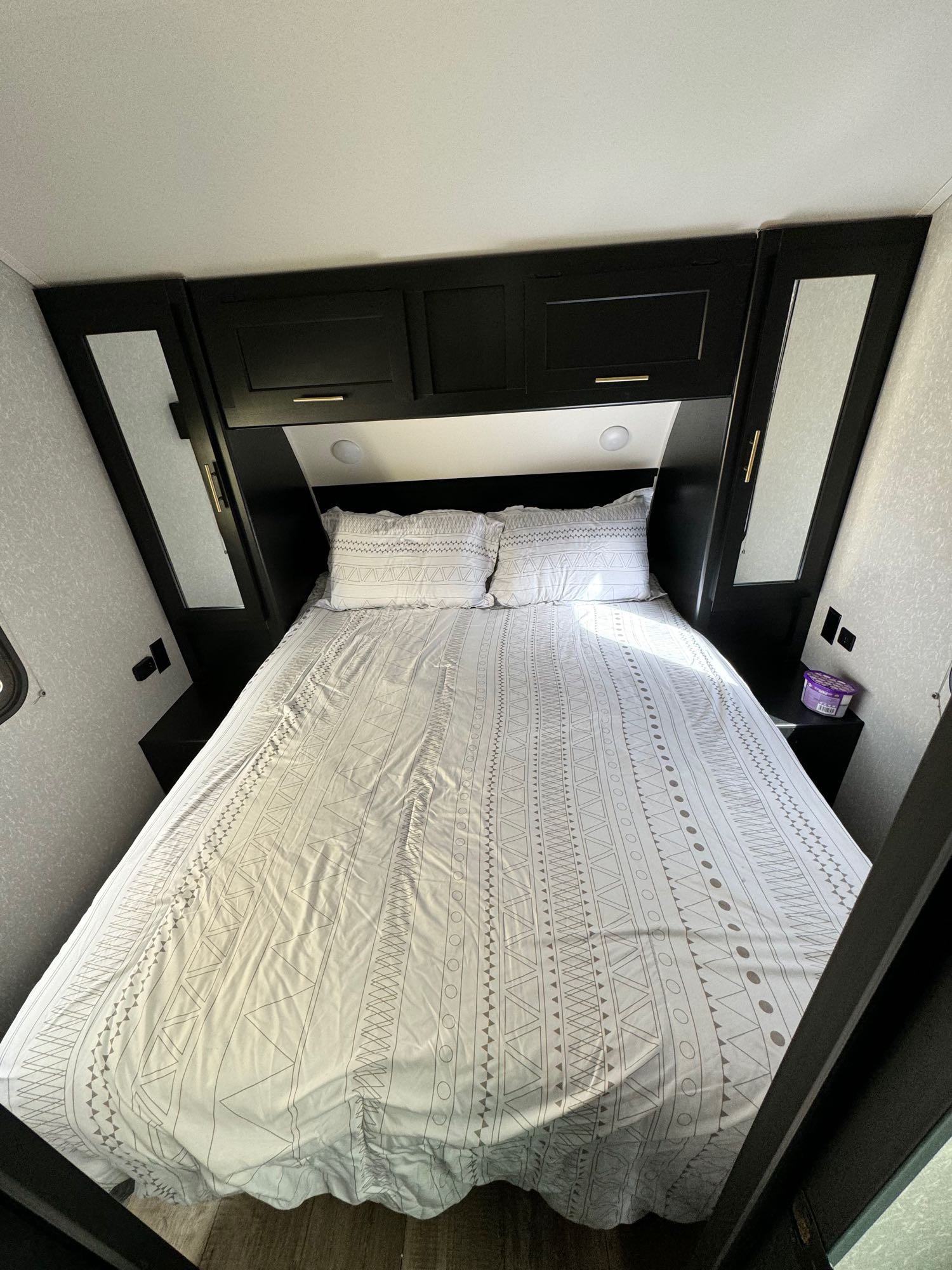 RV rental bedroom featuring a patterned bed, black overhead storage, and mirrored wardrobe cabinets. Bright and functional.. Greywolf 23MK 2022