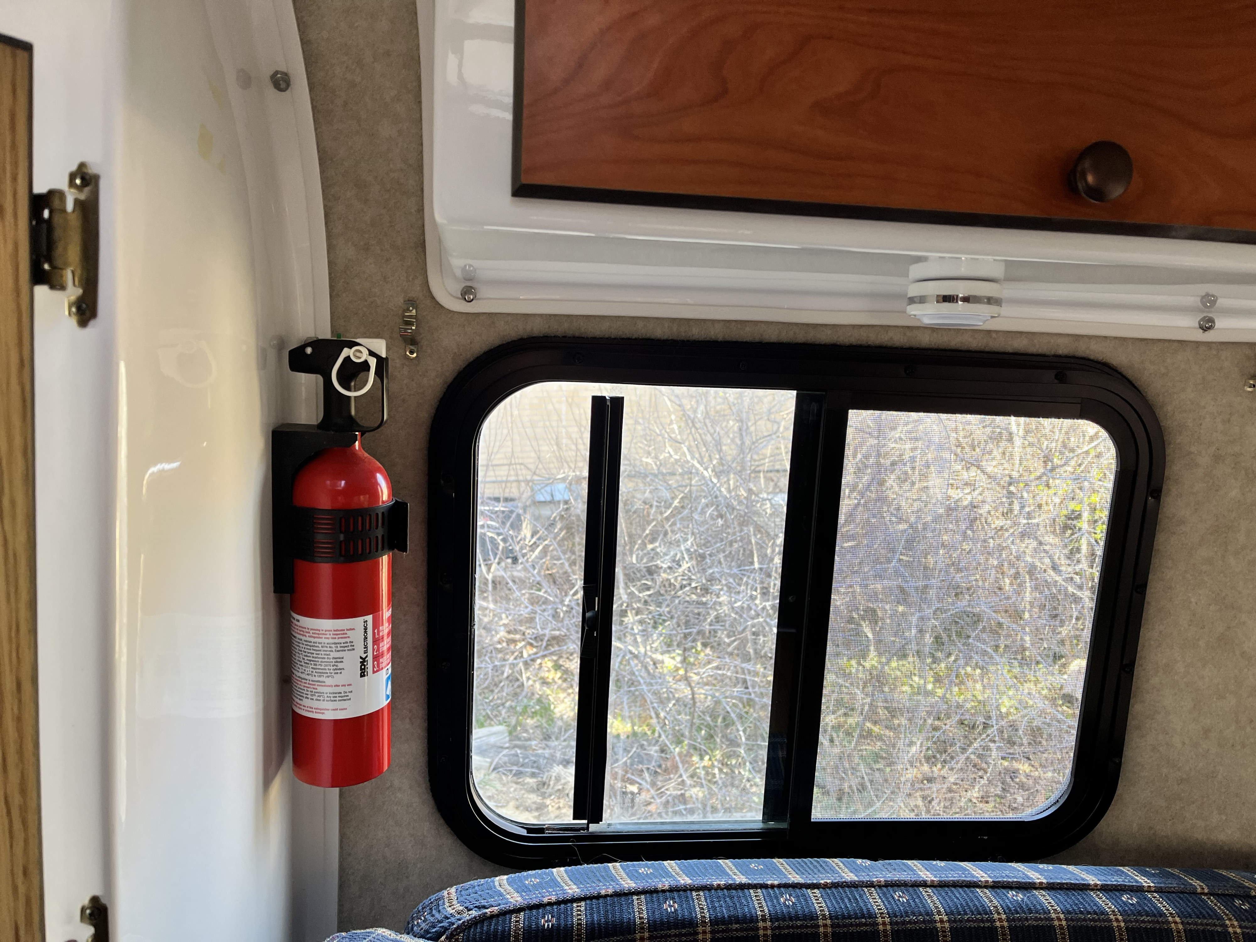 Essential RV rental safety: a fire extinguisher mounted beside a window with an outdoor view, cozy bed below.. Scamp Scamp Trailer 2004
