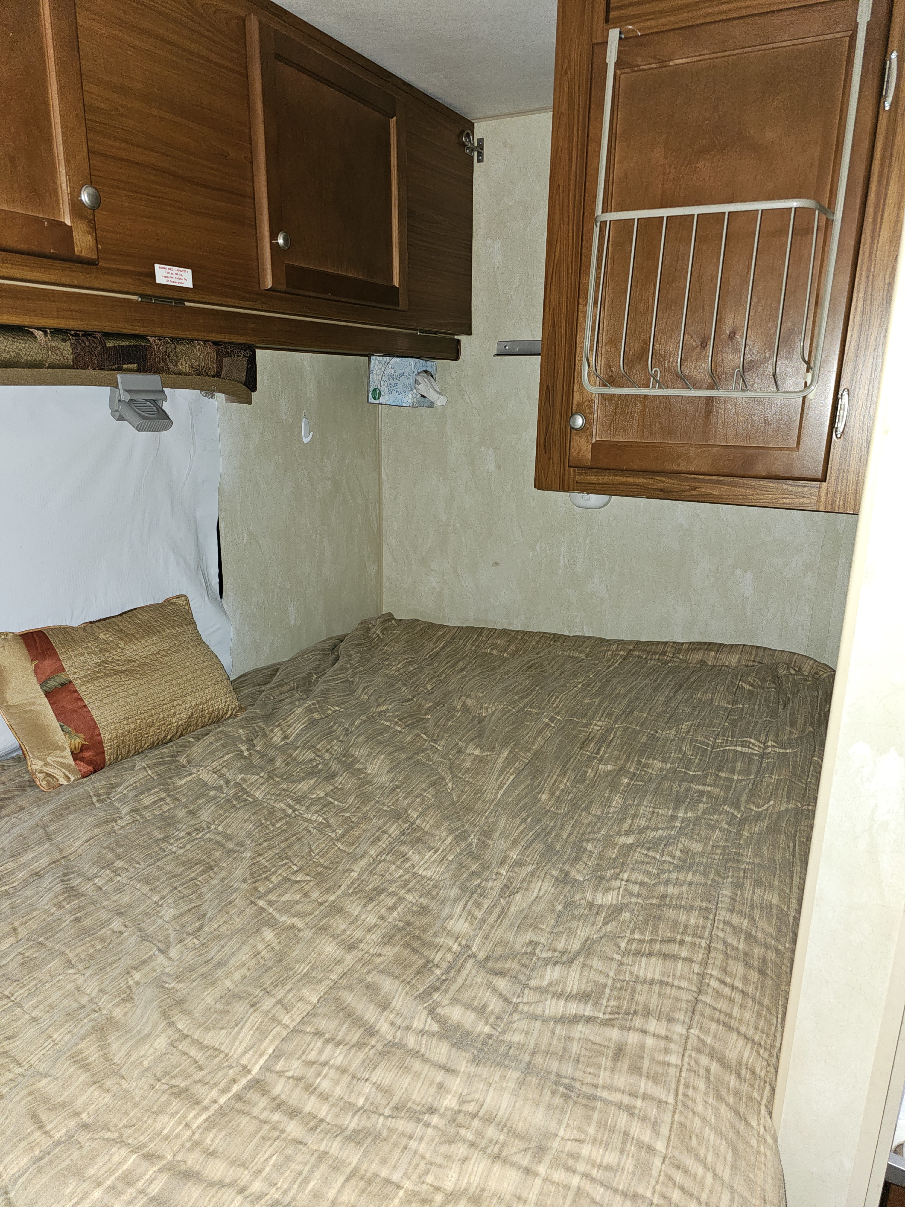 Compact RV rental bedroom featuring a textured bed, ample wood overhead cabinets, and smart wall-mounted storage solutions.. Nash Nash Trailer 2013