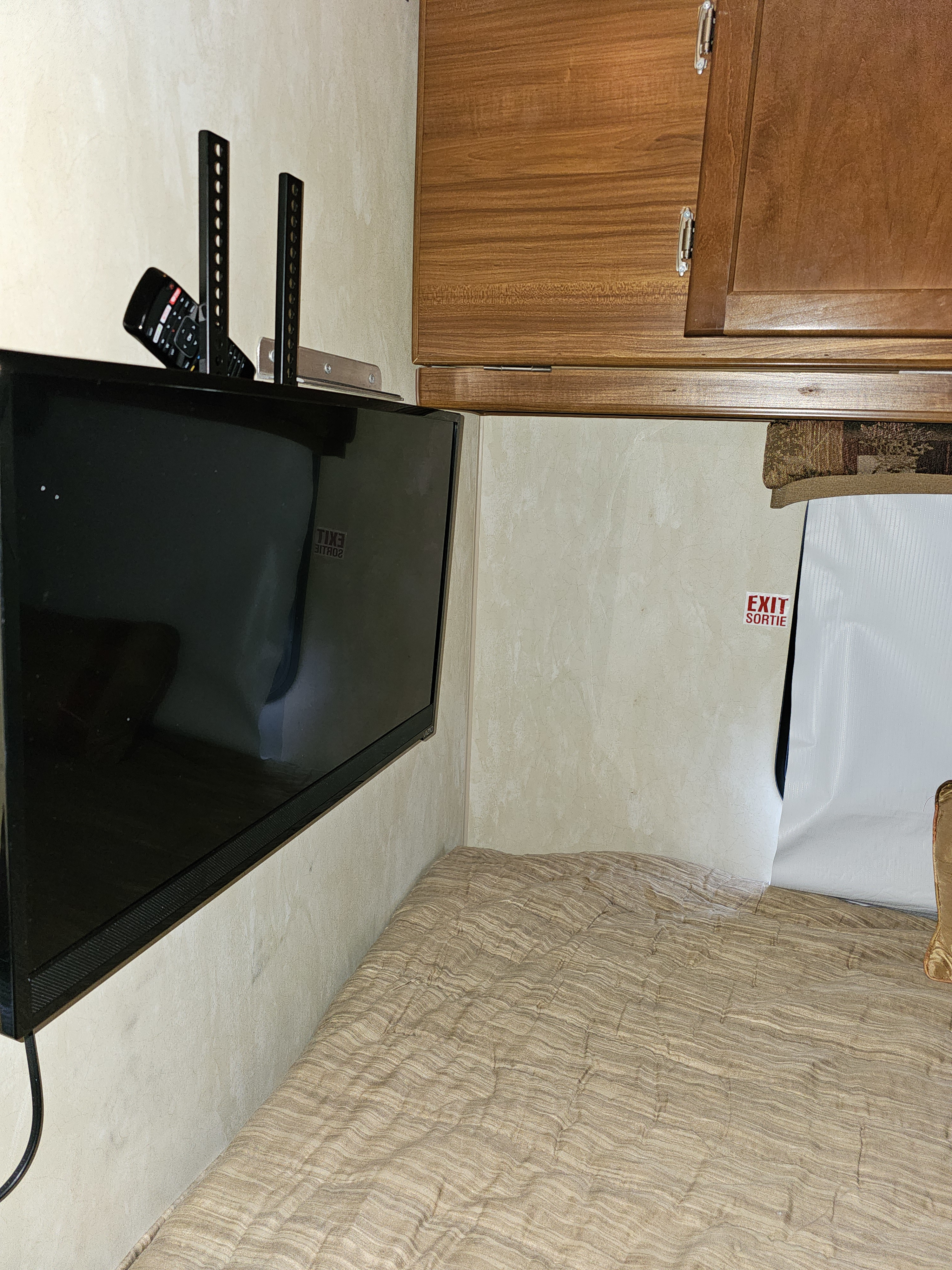 RV rental interior: wall-mounted TV with remote, comfortable bed with striped comforter, and an "EXIT SORTIE" sign.. Nash Nash Trailer 2013