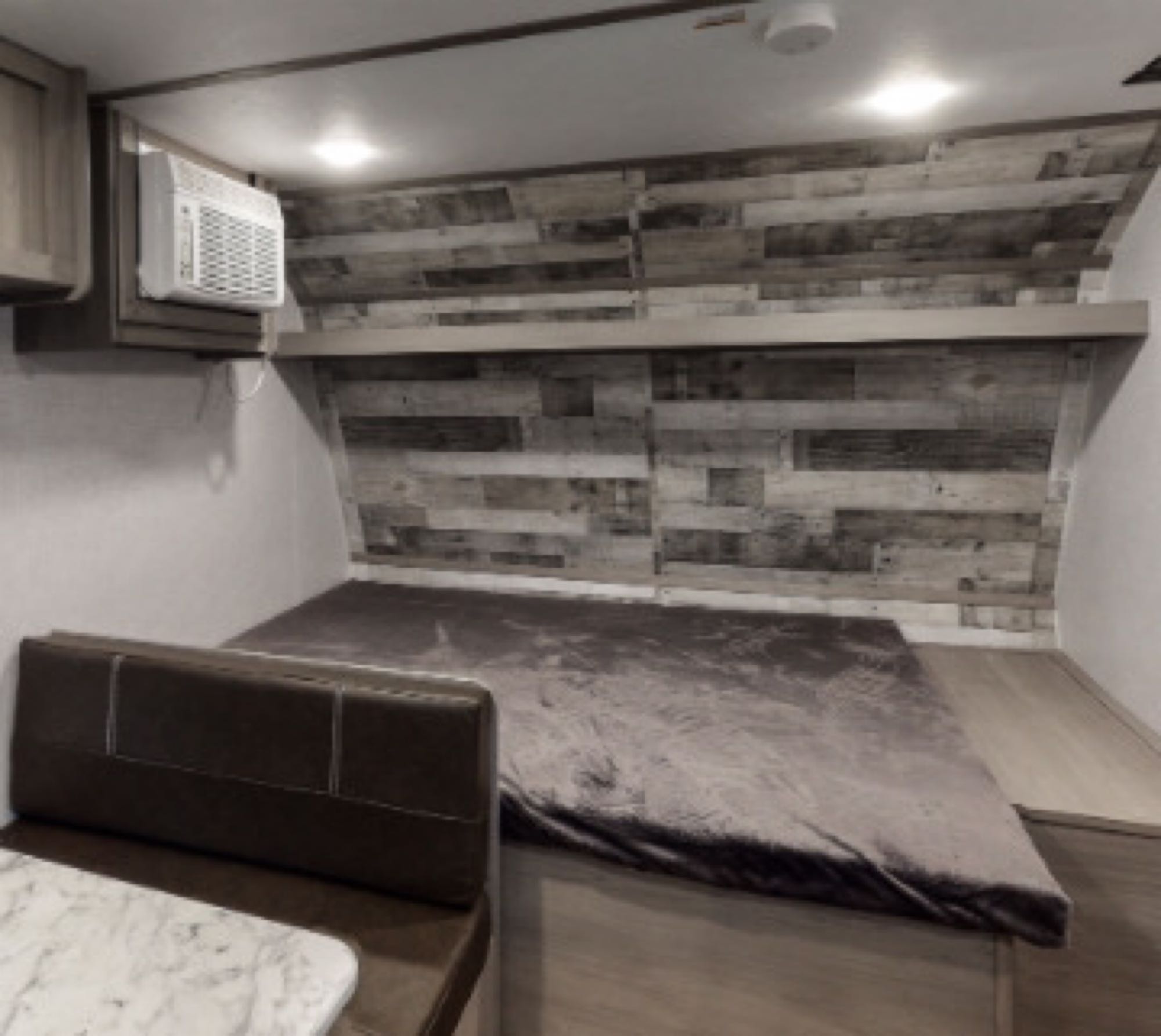 Discover this RV rental's cozy bedroom featuring a wood wall, AC unit, and a small dinette area with a brown bench.. Coleman Lantern 17b 2024