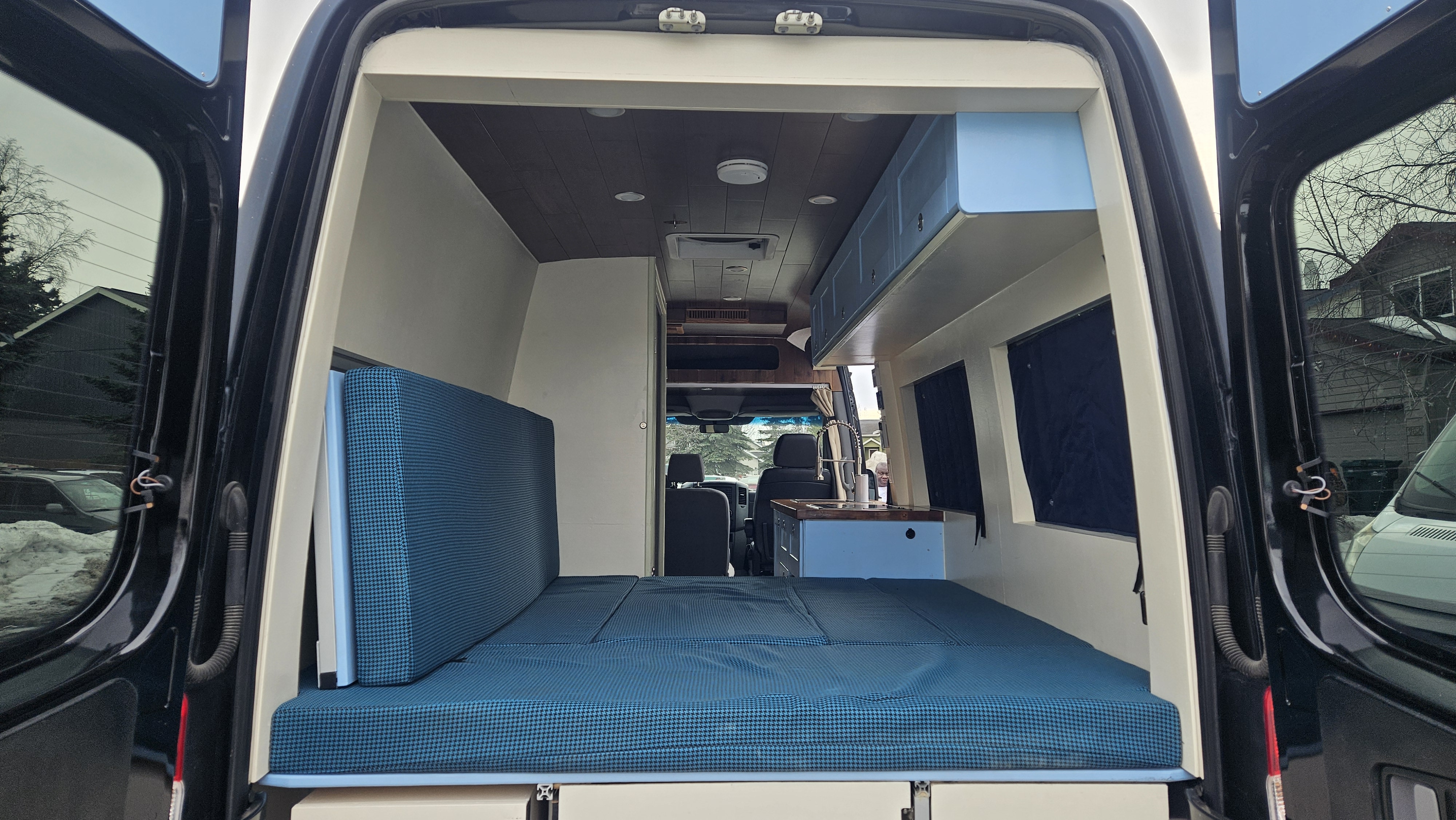 Experience this RV rental's versatile camper van interior: a convertible blue bed, compact kitchen, and overhead storage options.. Mercedes-Benz Sprinter 2015