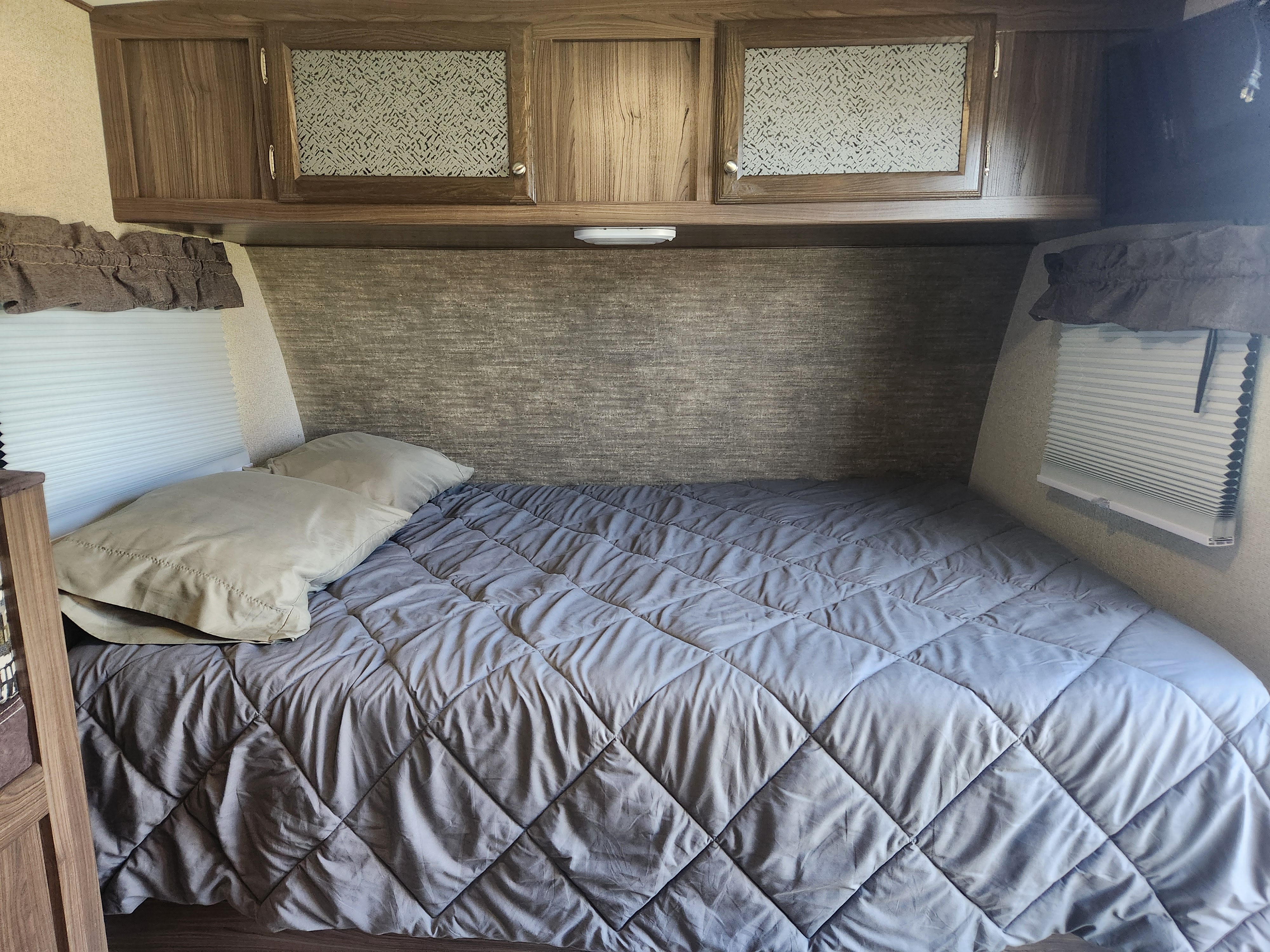 Cozy RV rental bedroom with a comfy quilted bed, pillows, and functional wooden cabinets. Ideal for compact travel.. Coachmen Apex Nano 2018