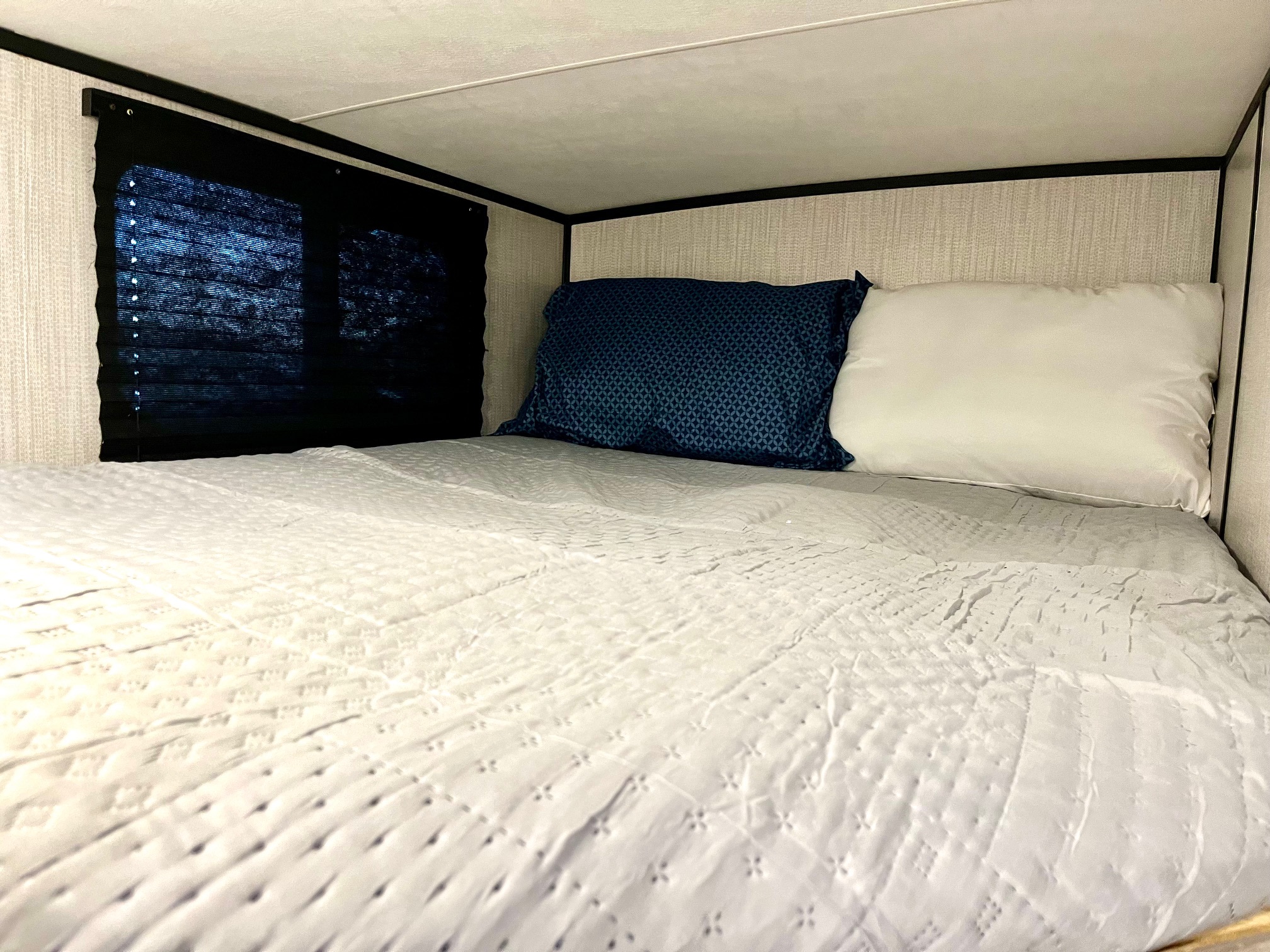 Cozy RV rental bunk bed interior, featuring two pillows, quilted bedding, and a closed window shade for privacy.. Heartland MALLARD 2021