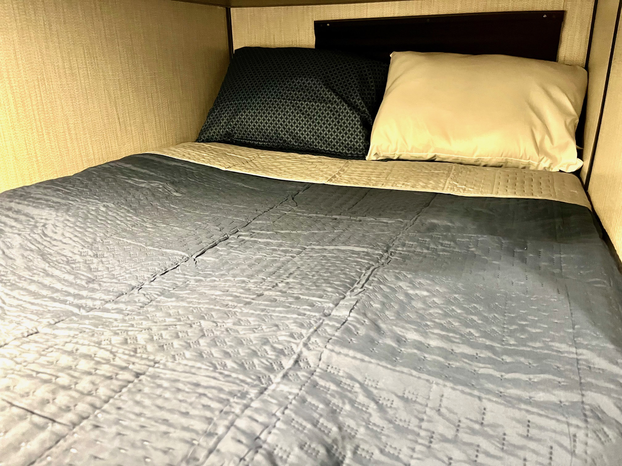 A cozy, made-up bed in an RV rental, featuring a grey quilted comforter, two pillows, and upholstered walls.. Heartland MALLARD 2021