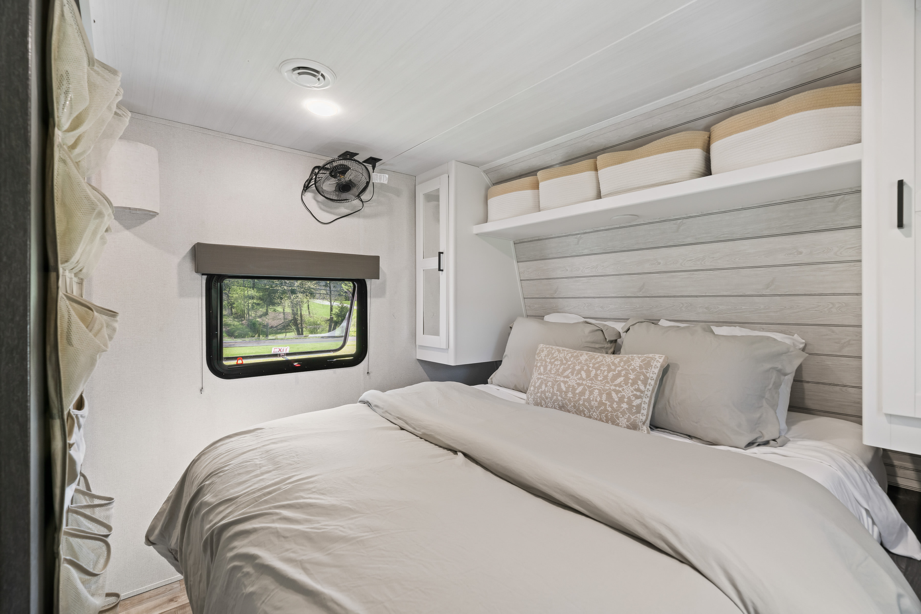 Cozy RV rental bedroom featuring a comfy bed, window with nature view, wall fan, and integrated storage.. Keystone RV Hideout 2022