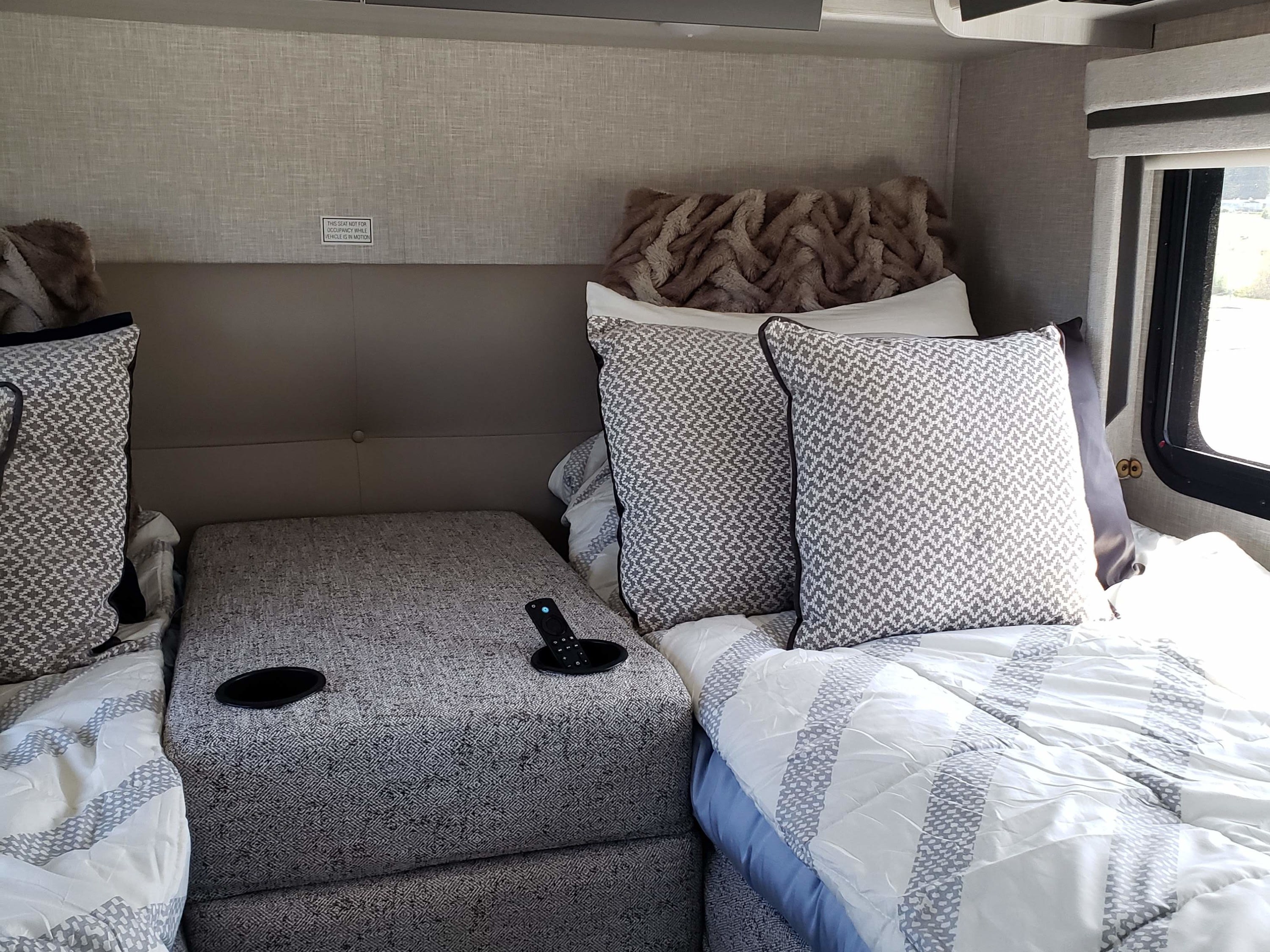 Inside an RV rental: Relaxing twin beds with patterned pillows, white comforters, and a central console with cup holders.. Thor Compass 2024