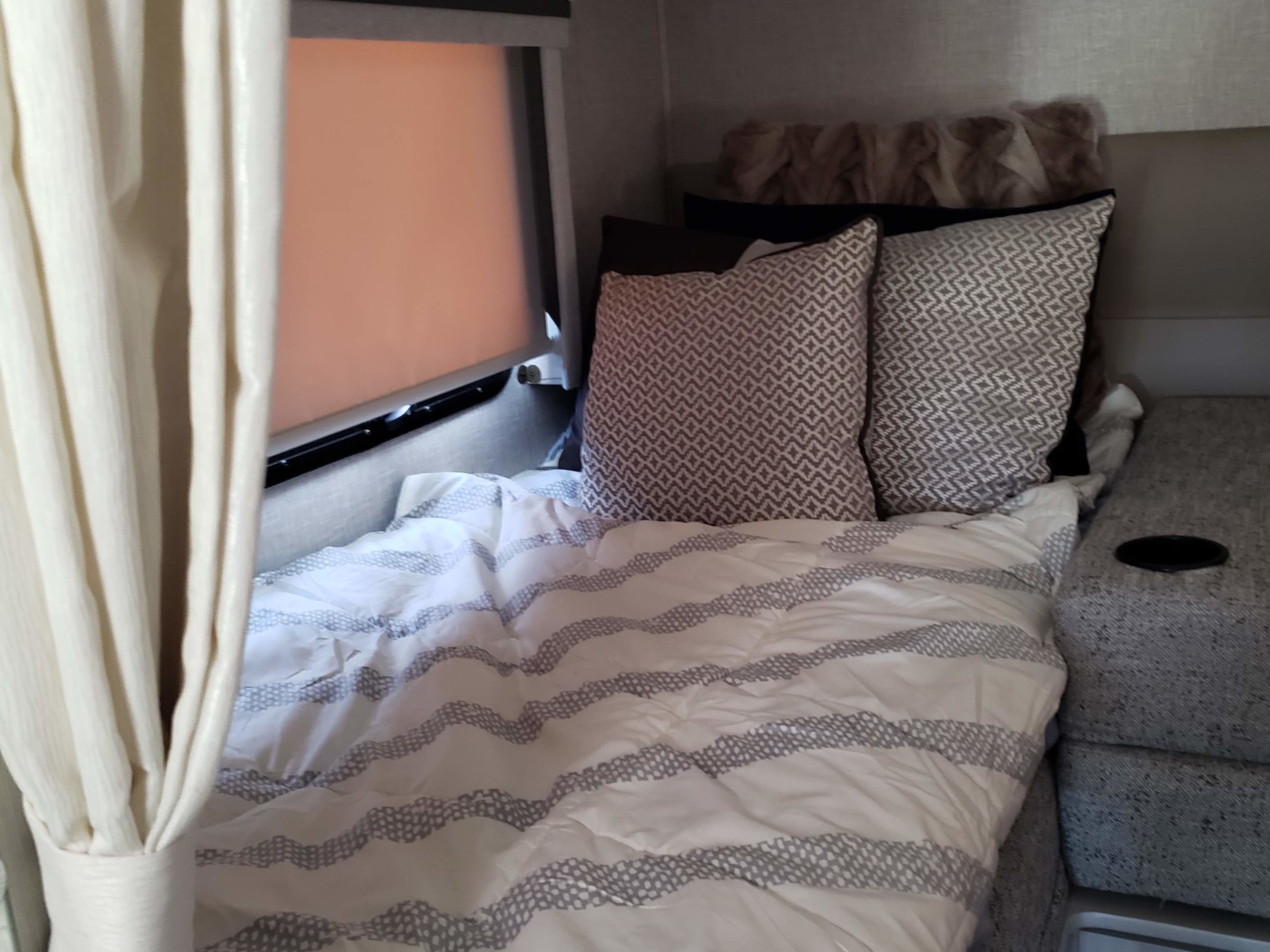 Cozy RV rental bedroom featuring white and grey striped bedding, plush pillows, and a window, ideal for comfortable travel.. Thor Compass 2024