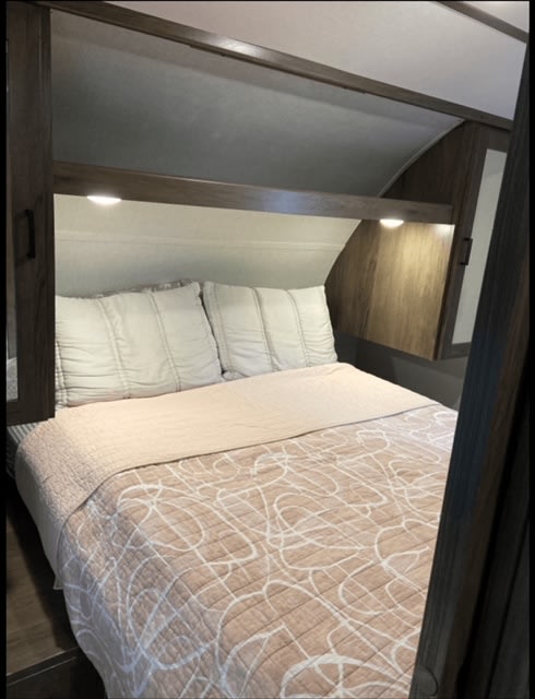 RV rental bedroom: A cozy bed with soft bedding, pillows, overhead storage, and reading lights for comfortable travels.. Forest River Tracer LE 2020