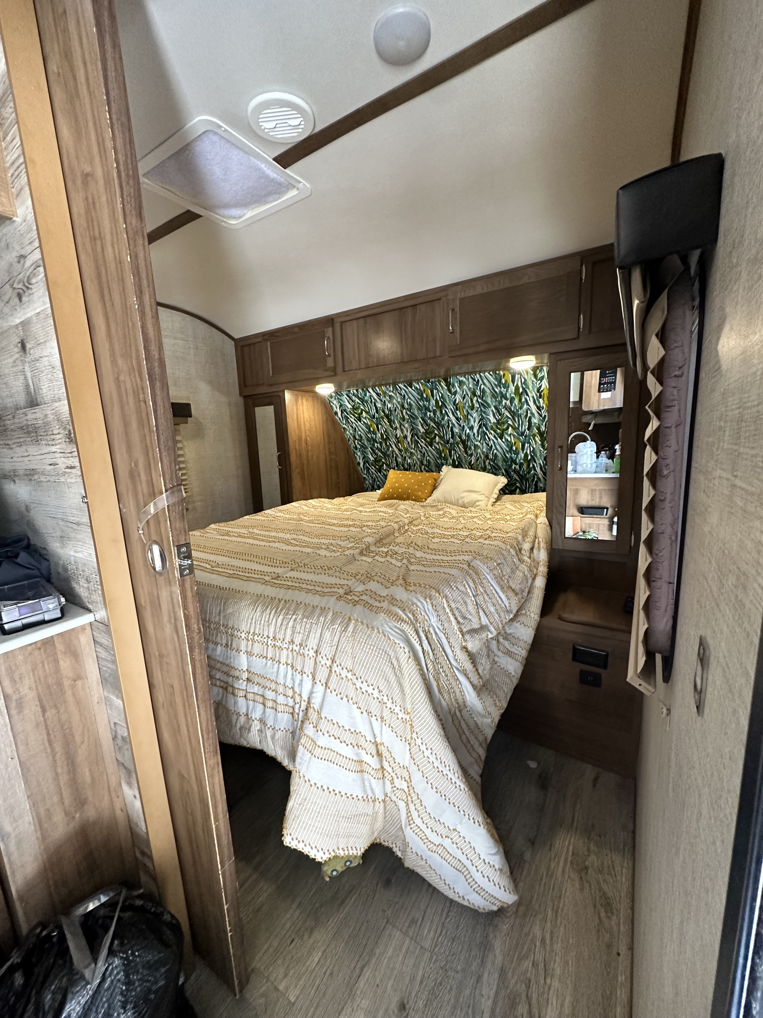 Inside an RV rental: a cozy bedroom featuring an elegant bed, overhead cabinets, and a vibrant leaf accent wall.. Gulf Stream Envision 2020