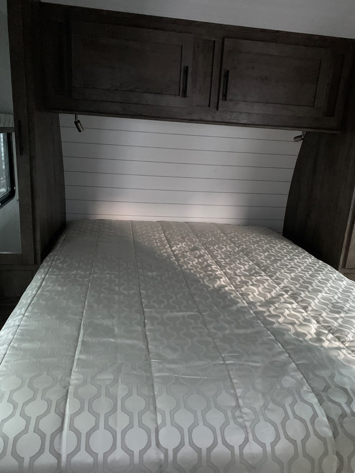 Cozy RV rental bedroom with shiplap headboard, overhead storage, reading lights, and patterned comforter.. Forest River Stealth 2021