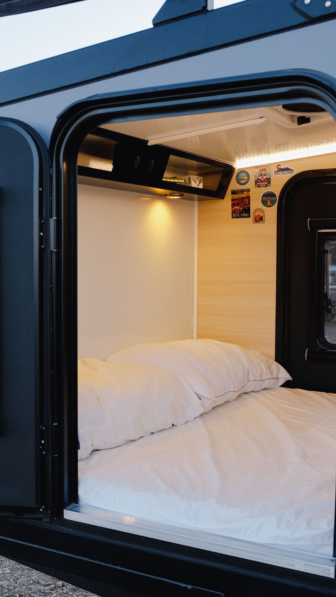 An inviting bed inside a compact RV rental, featuring white linens and warm lighting, ready for adventure.. Boreas XT 2023