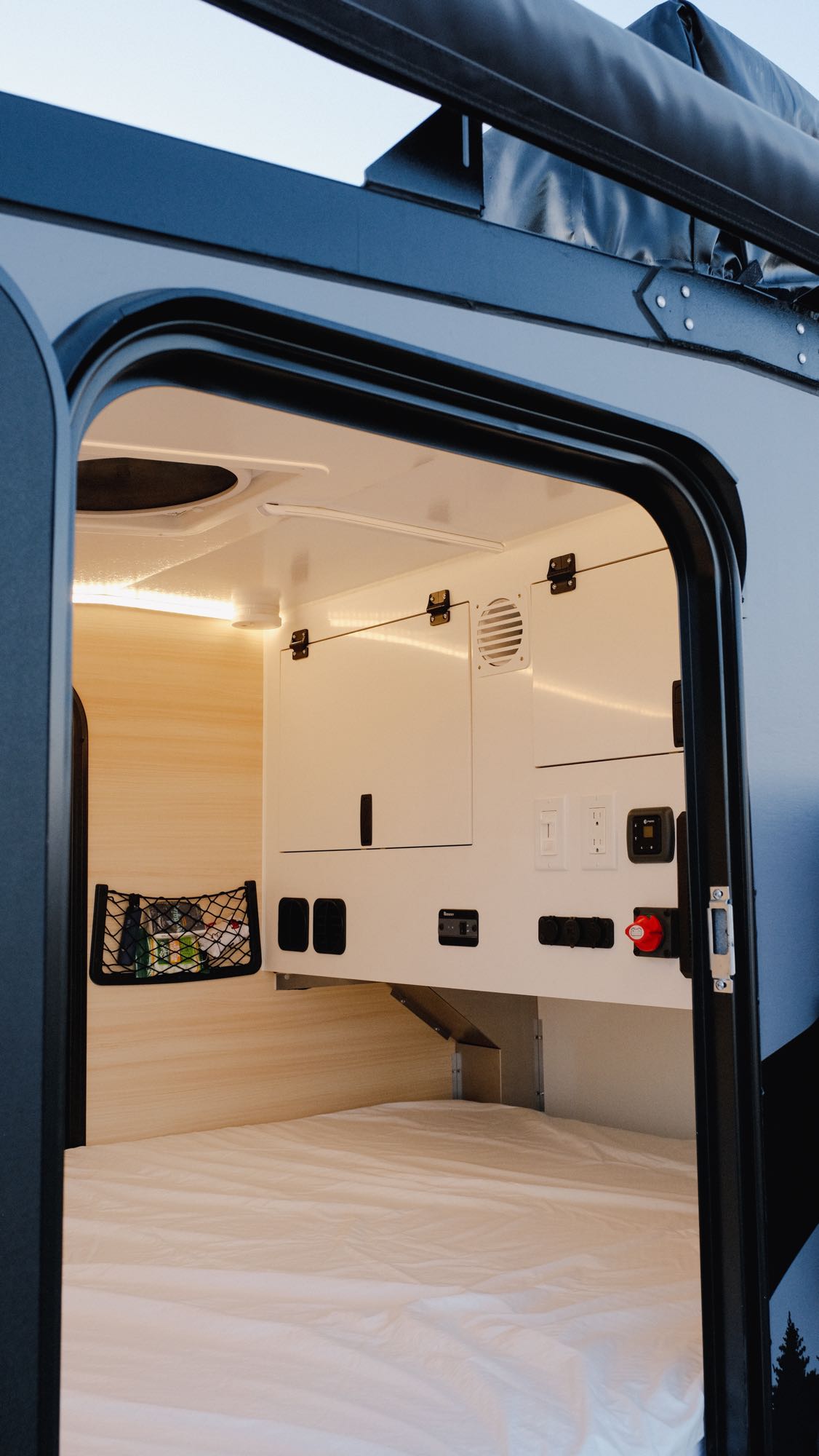 Cozy RV rental interior shows a clean bed, warm LED lighting, and a practical control panel with storage, ready for comfortable travel.. Boreas XT 2023