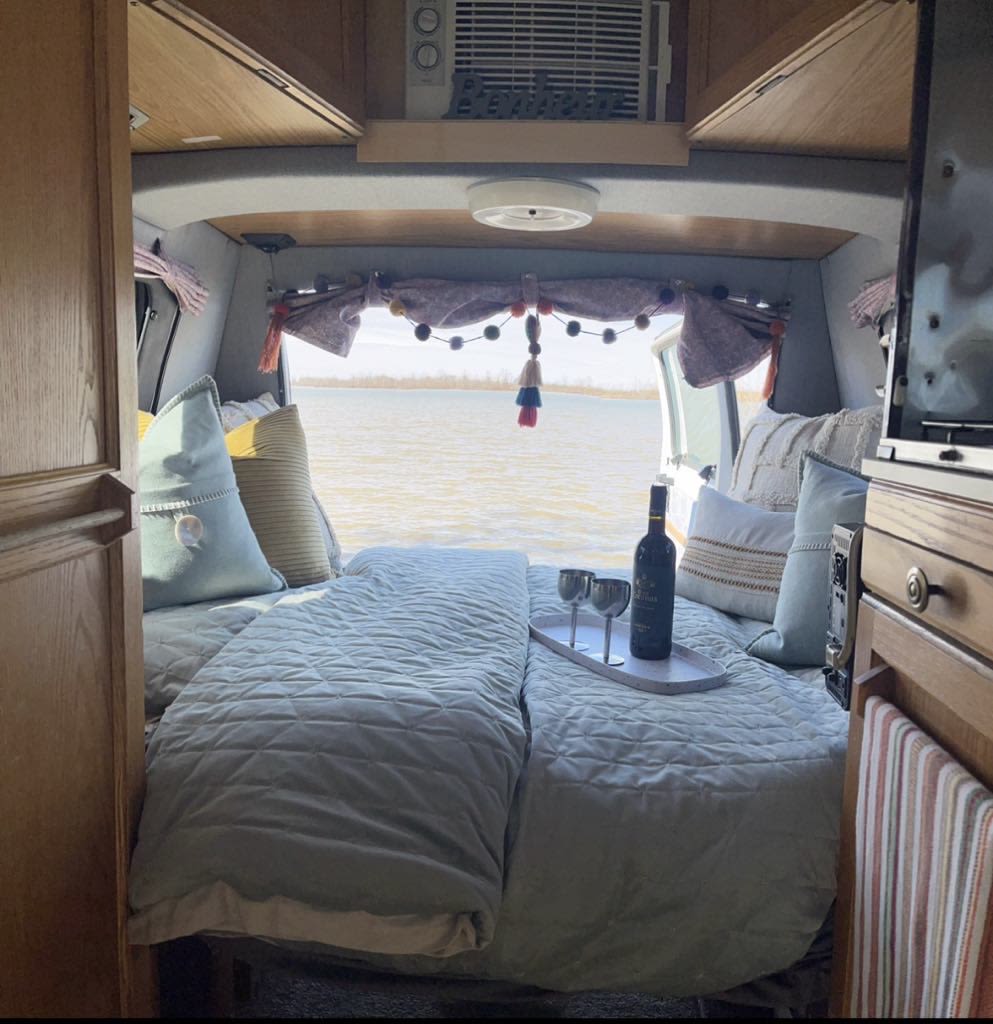 RV rental interior: a cozy bed with wine setup, offering stunning lake views from the open back doors. Perfect for glamping!. Roadtrek 190 Versatile 1995