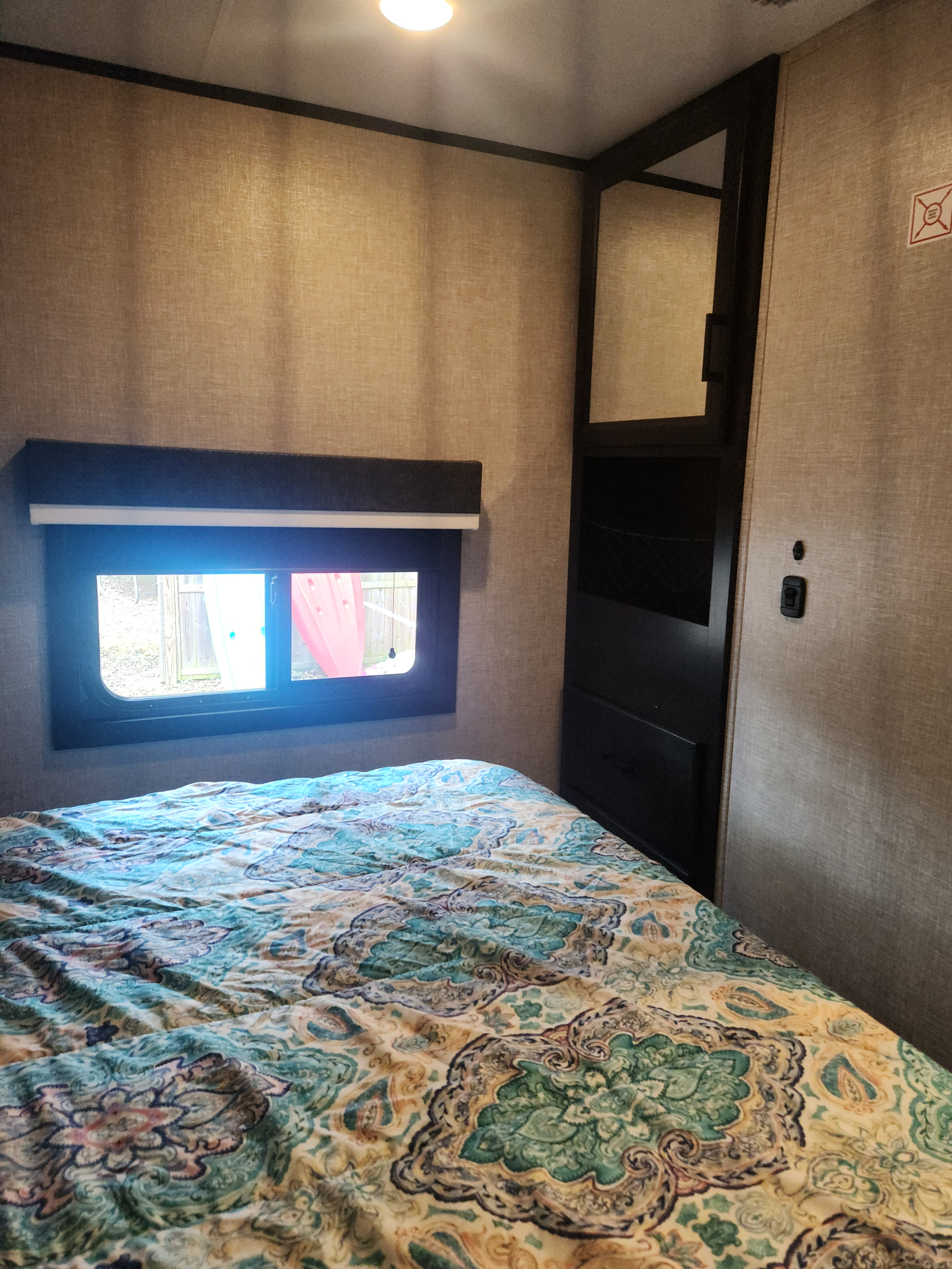 Cozy RV rental bedroom featuring a bed with a patterned quilt, window with backyard view, and built-in storage.. Jayco Eagle HT 2022