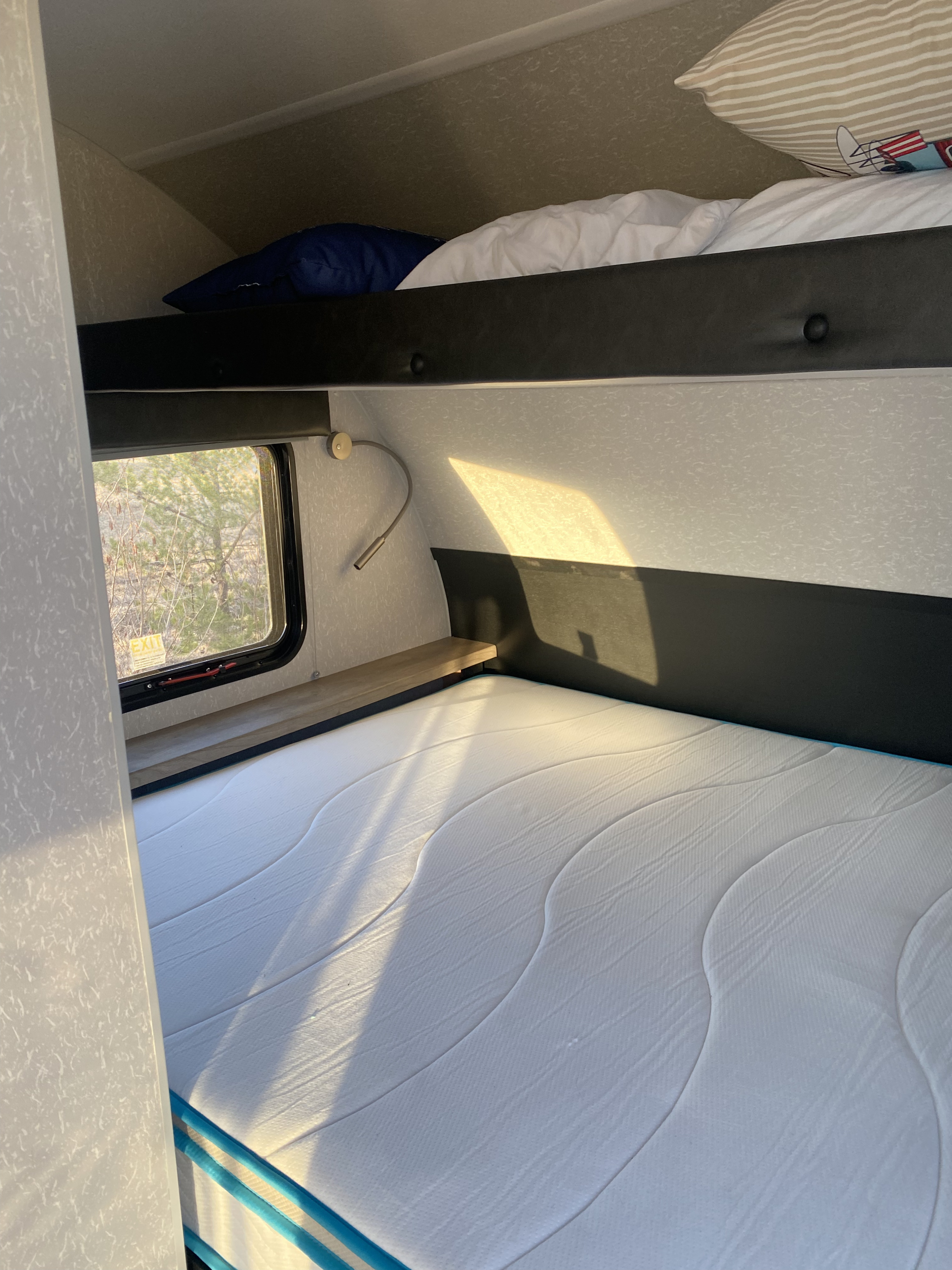 Cozy RV rental bunk beds with a new mattress, sunlit window, and reading lamp. Ideal for compact living.. Forest River Cherokee Wolf Pup 2022
