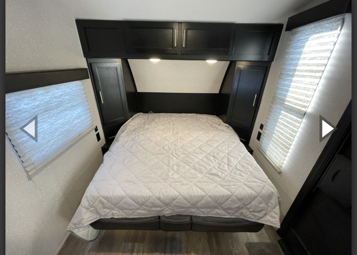 Experience comfort in this RV rental's compact bedroom, featuring a large bed, dark wood cabinets, and two side windows with blinds.. Forest River Cherokee Wolf Pup 2022