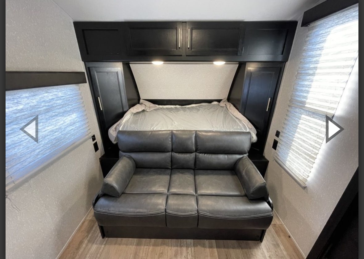 RV rental interior: comfy gray sofa facing a bed with black overhead cabinets & side windows with blinds.. Forest River Cherokee Wolf Pup 2022