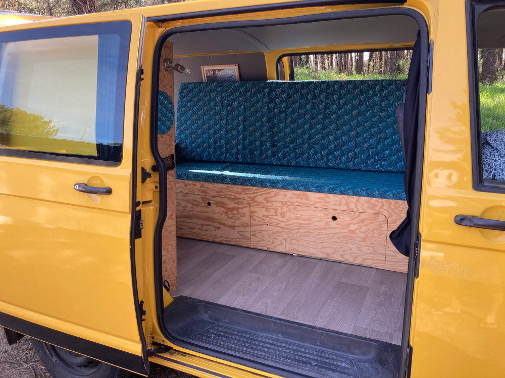 Yellow RV rental's cozy interior: custom bench with teal cushions, wood storage, and laminate floor. Ready for travel!. Volkswagen Transporter T5 2012