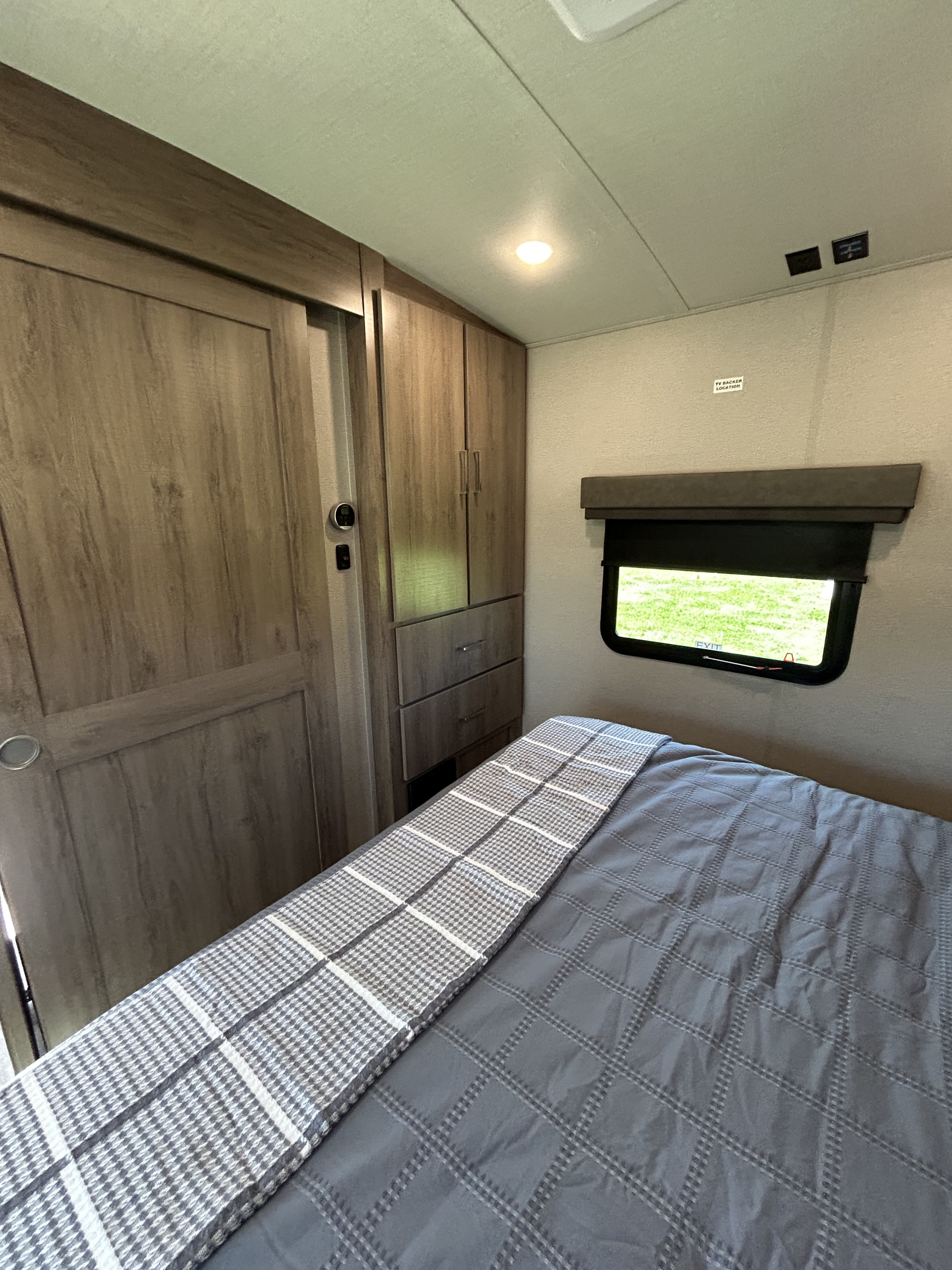 Inside an RV rental: a modern bedroom featuring a bed, wood cabinetry, and a window with a view.. Grand Design Imagine 2022
