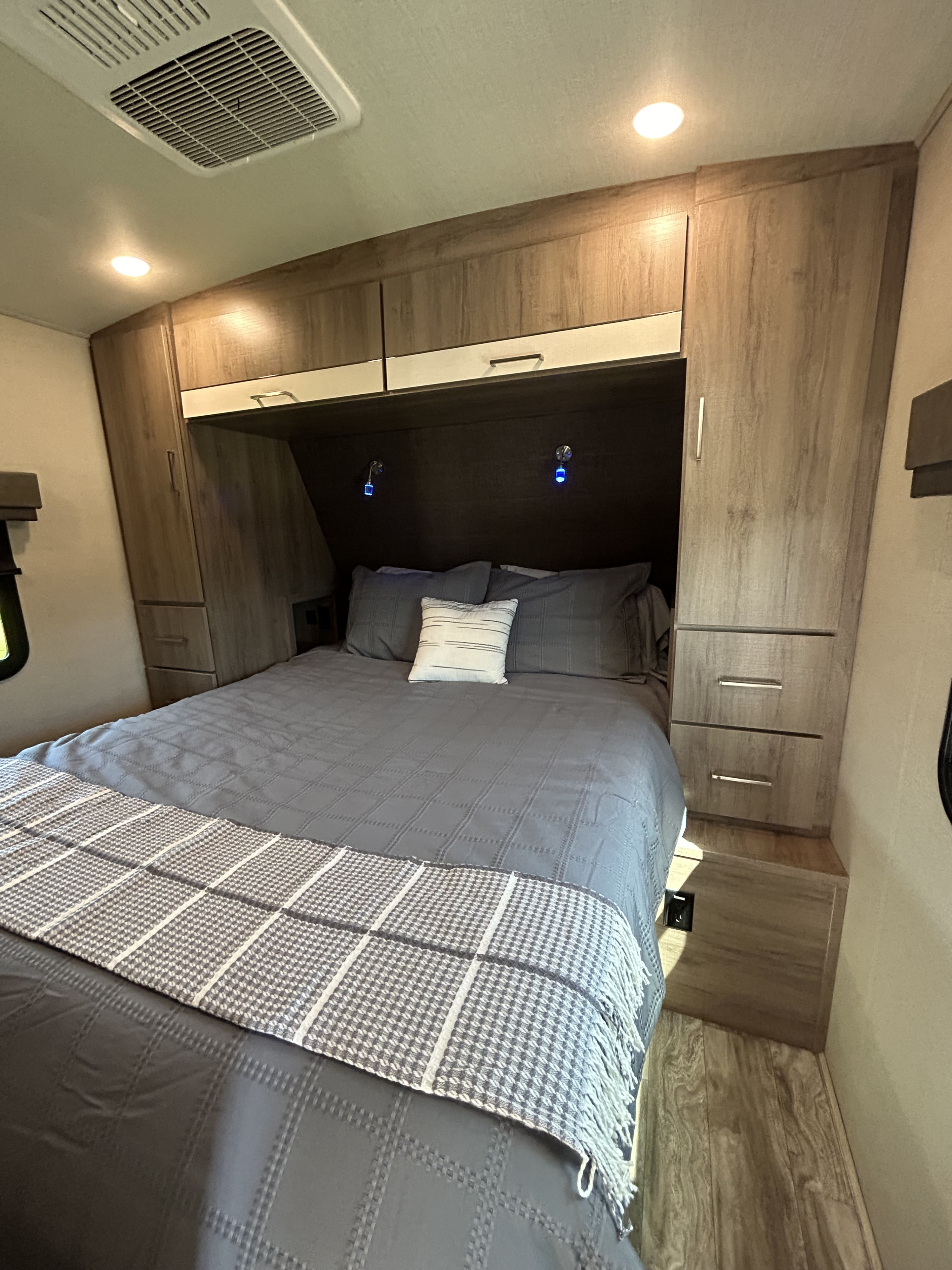 Modern RV rental bedroom with a queen bed, overhead cabinetry, built-in storage, and ambient lighting.. Grand Design Imagine 2022