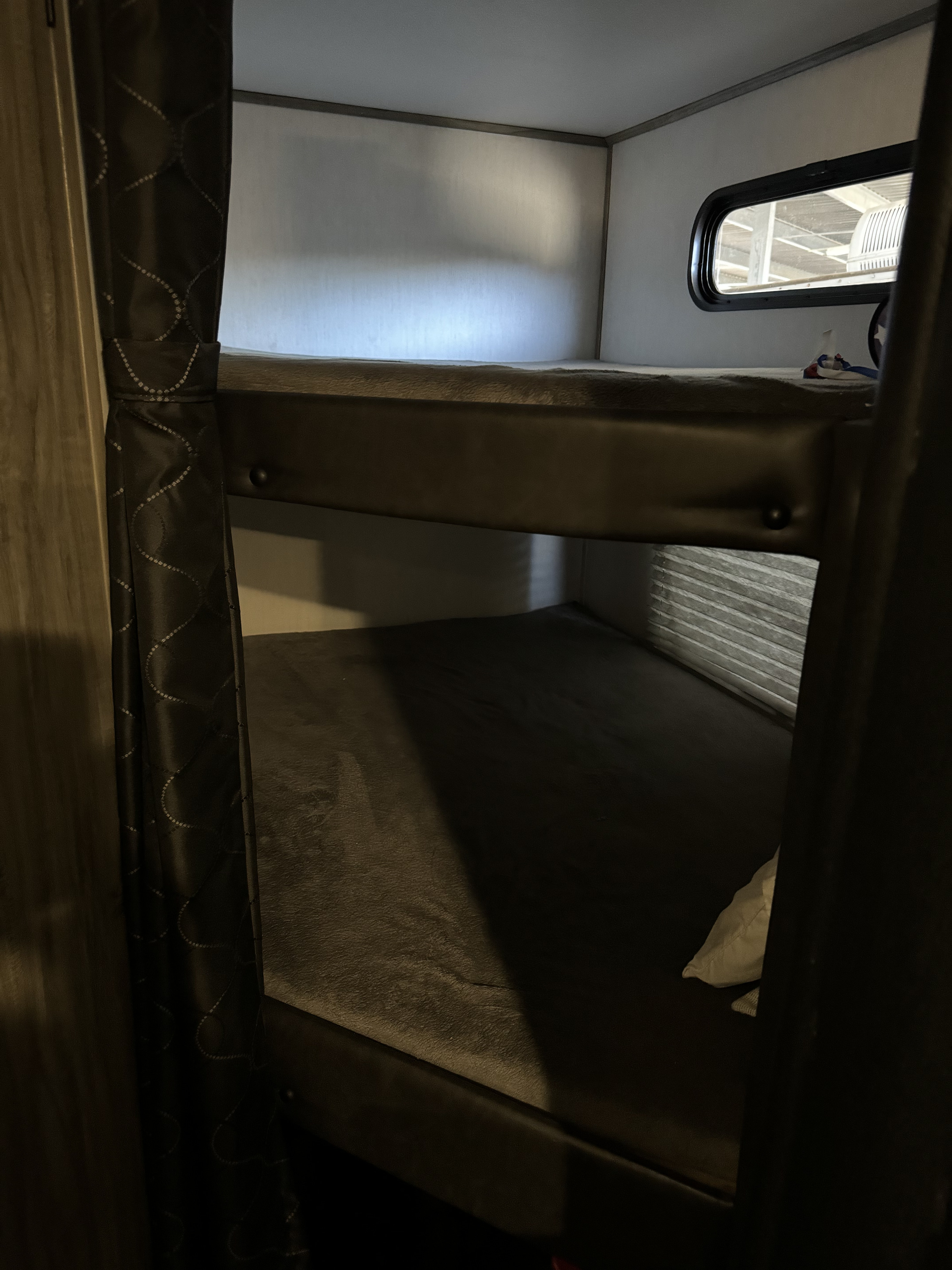 RV rental's dark, cozy bunk beds. The top bunk features a window with an industrial view, offering a compact sleeping area.. Forest River Cherokee Alpha Wolf 2022