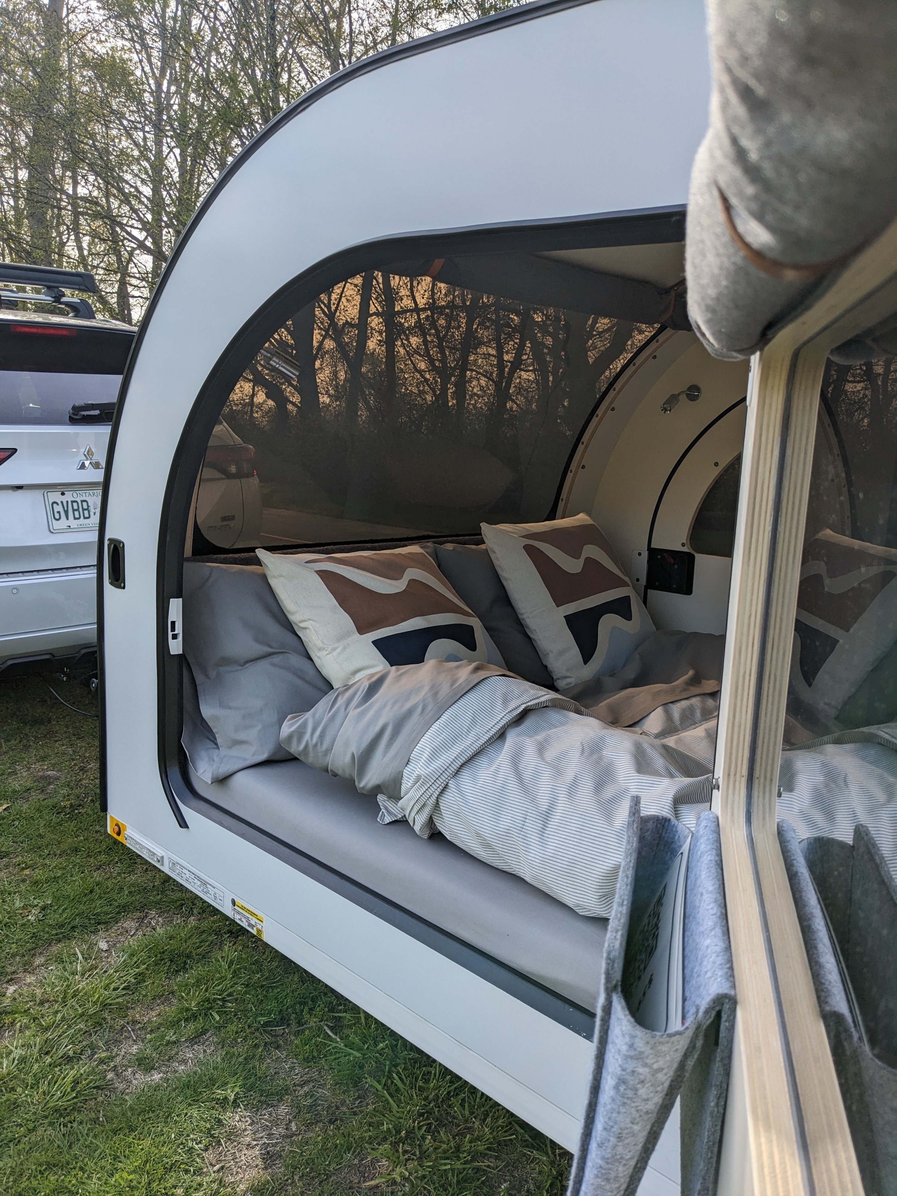 Cozy teardrop rv rental interior showing bed, pillows, and view through the large window. Perfect compact camping.. droplet XL 2023