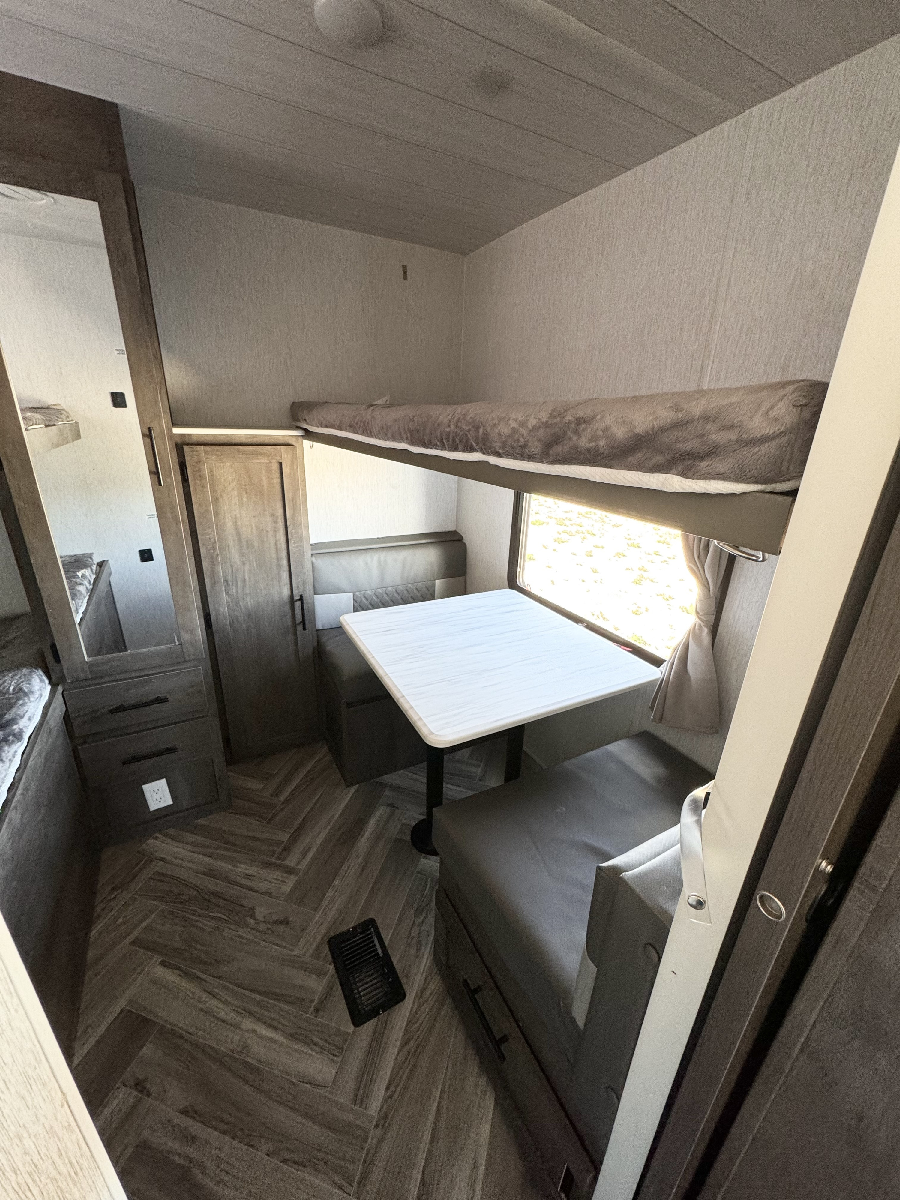 Interior of an RV rental showing a dinette with bench seating, upper bunk bed, and mirrored storage. Ready for road trips!. Forest River Wildwood 2022