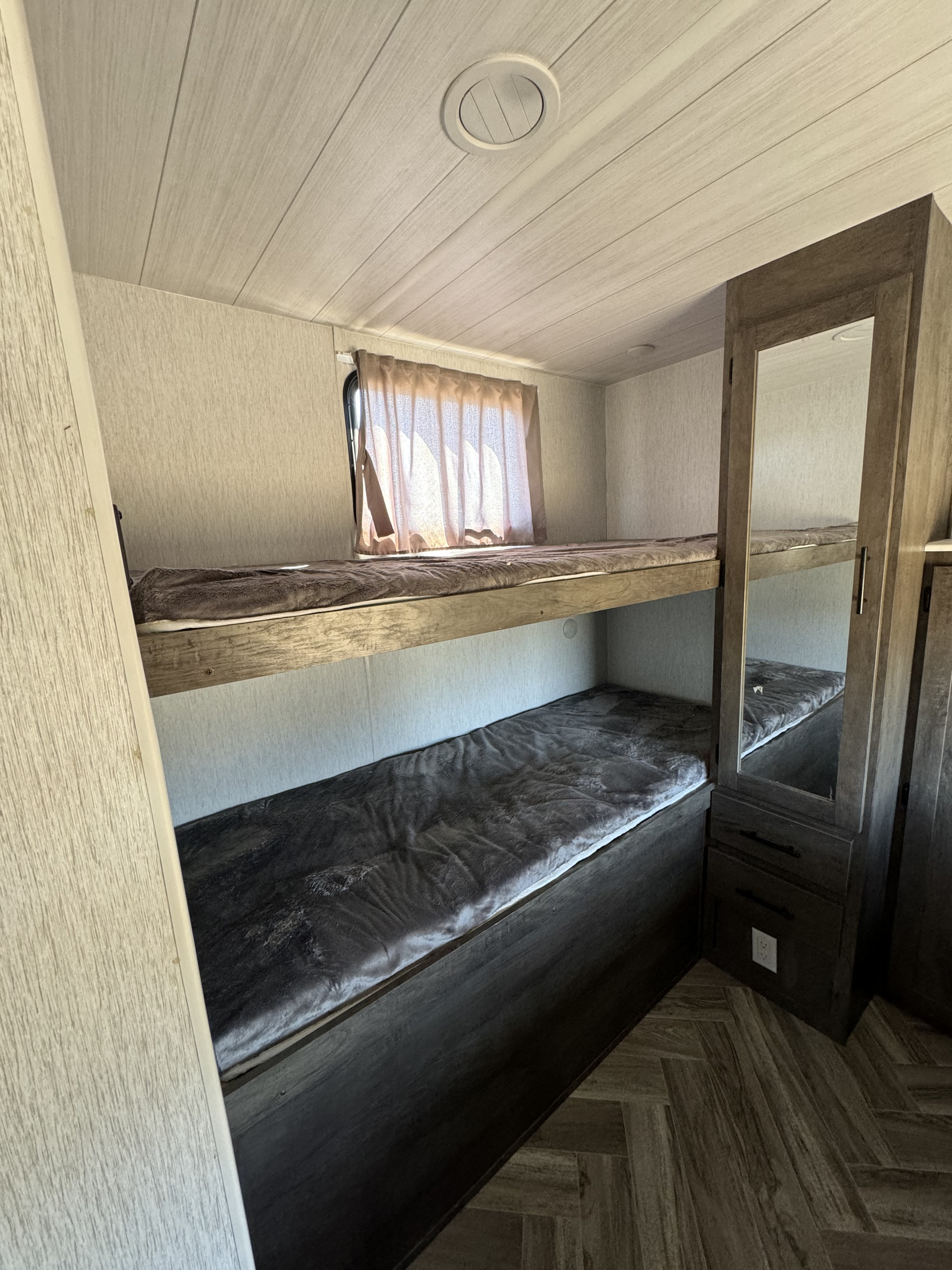 Cozy RV rental bunk beds with plush bedding, a window, and a mirrored wardrobe for comfortable camping.. Forest River Wildwood 2022
