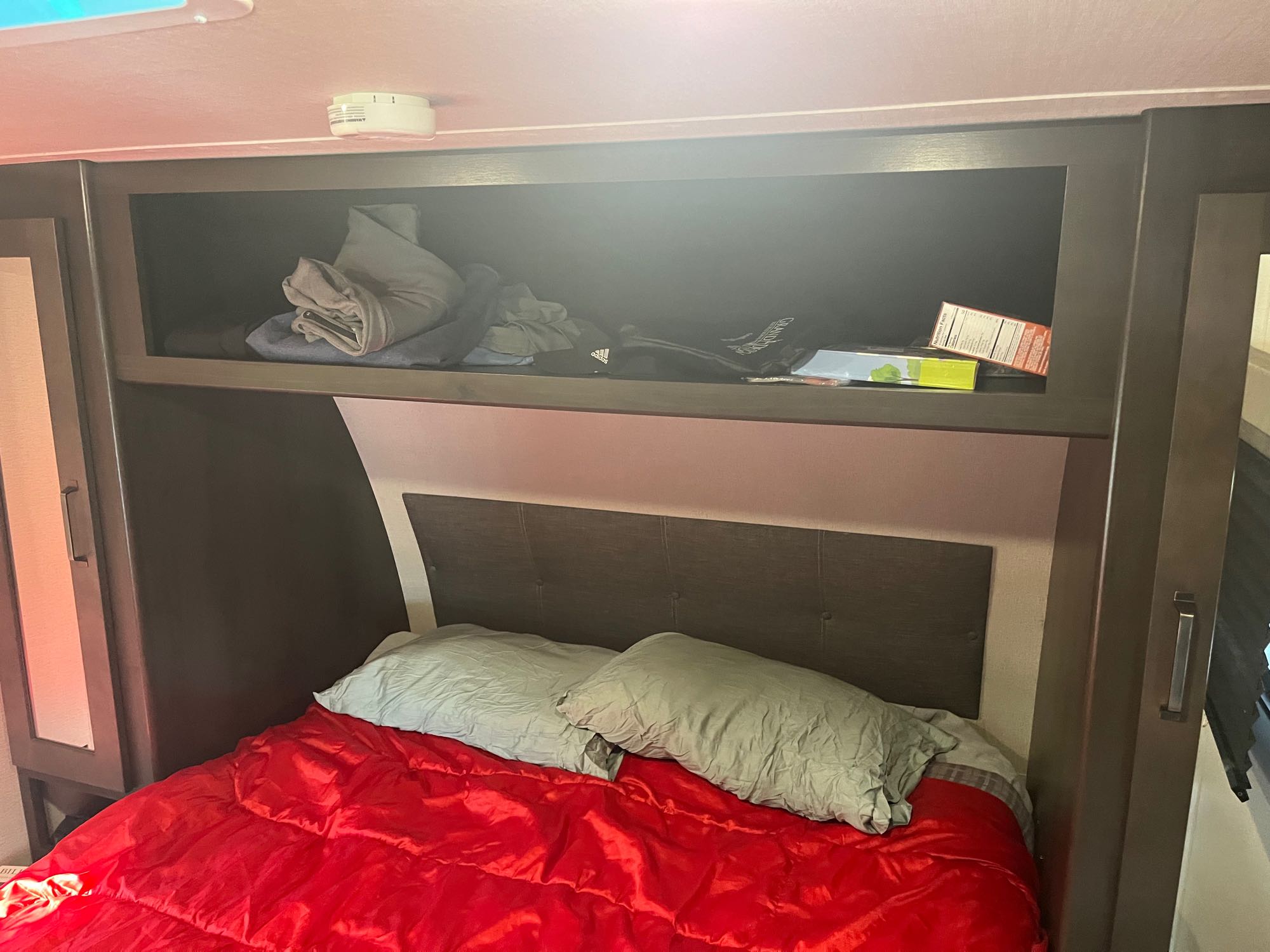 An RV rental bedroom with a comfy red bed & pillows, plus practical overhead storage for travel essentials.. Grand Design Transcend Xplor 2020