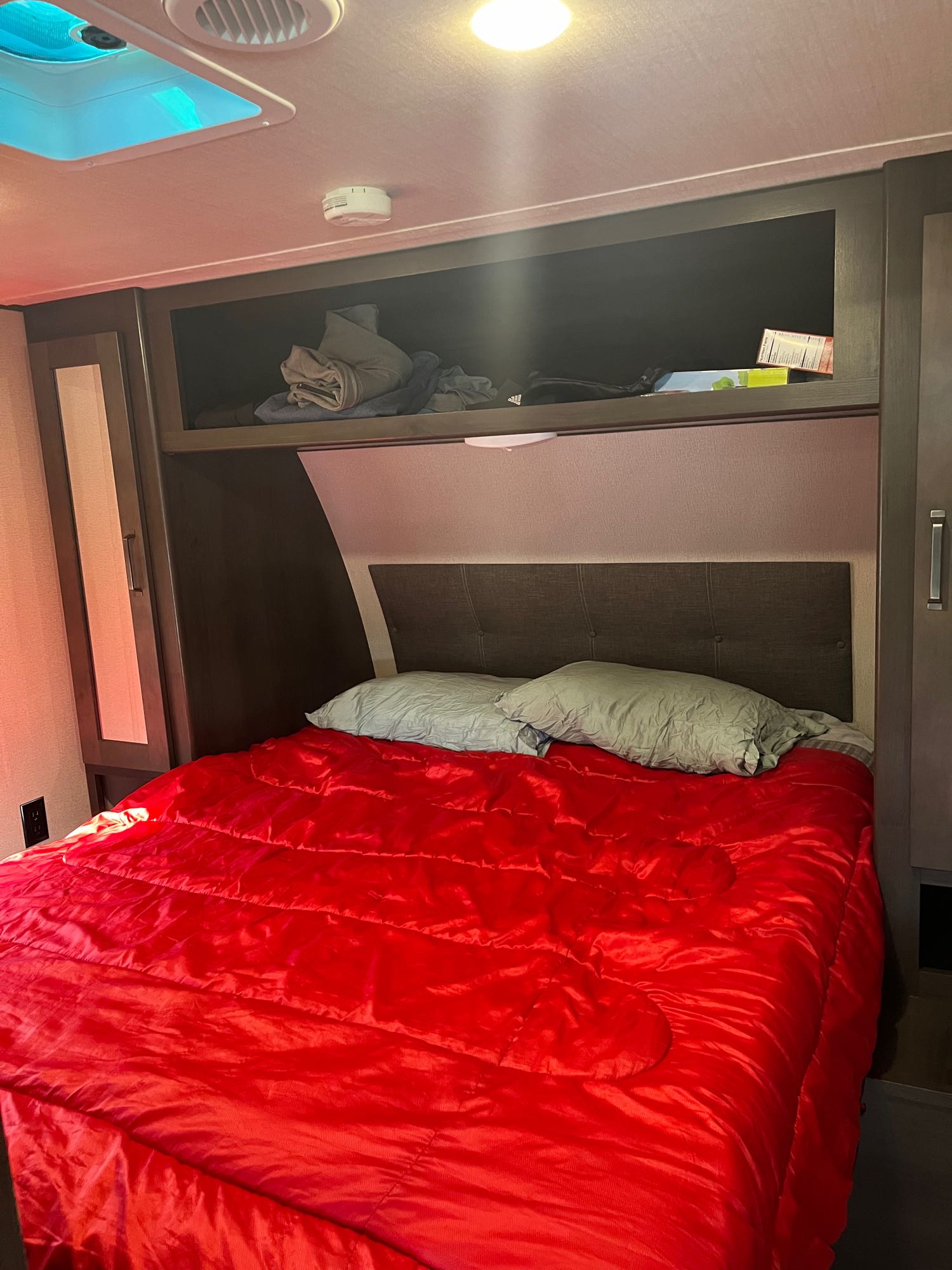 This RV rental bedroom offers a comfy red bed, pillows, and convenient overhead storage.. Grand Design Transcend Xplor 2020