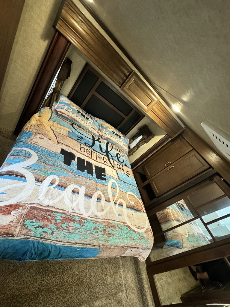 Cozy RV rental bedroom featuring a bed with a "Life is better at THE Beach" comforter, showcasing comfortable interior.. Keystone RV Fuzion Chrome Toy Hauler 2016