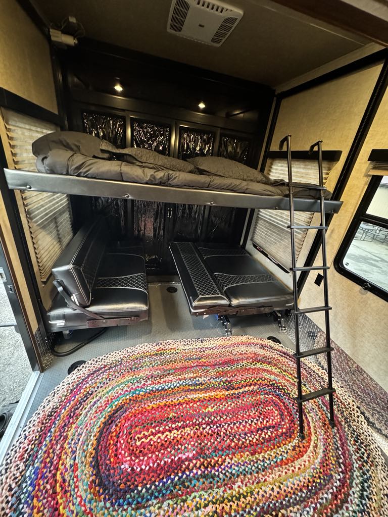 This RV rental interior features a cozy bunk bed, versatile lower seating/beds, and a vibrant braided rug. Ideal for adventurers.. Keystone RV Fuzion Chrome Toy Hauler 2016