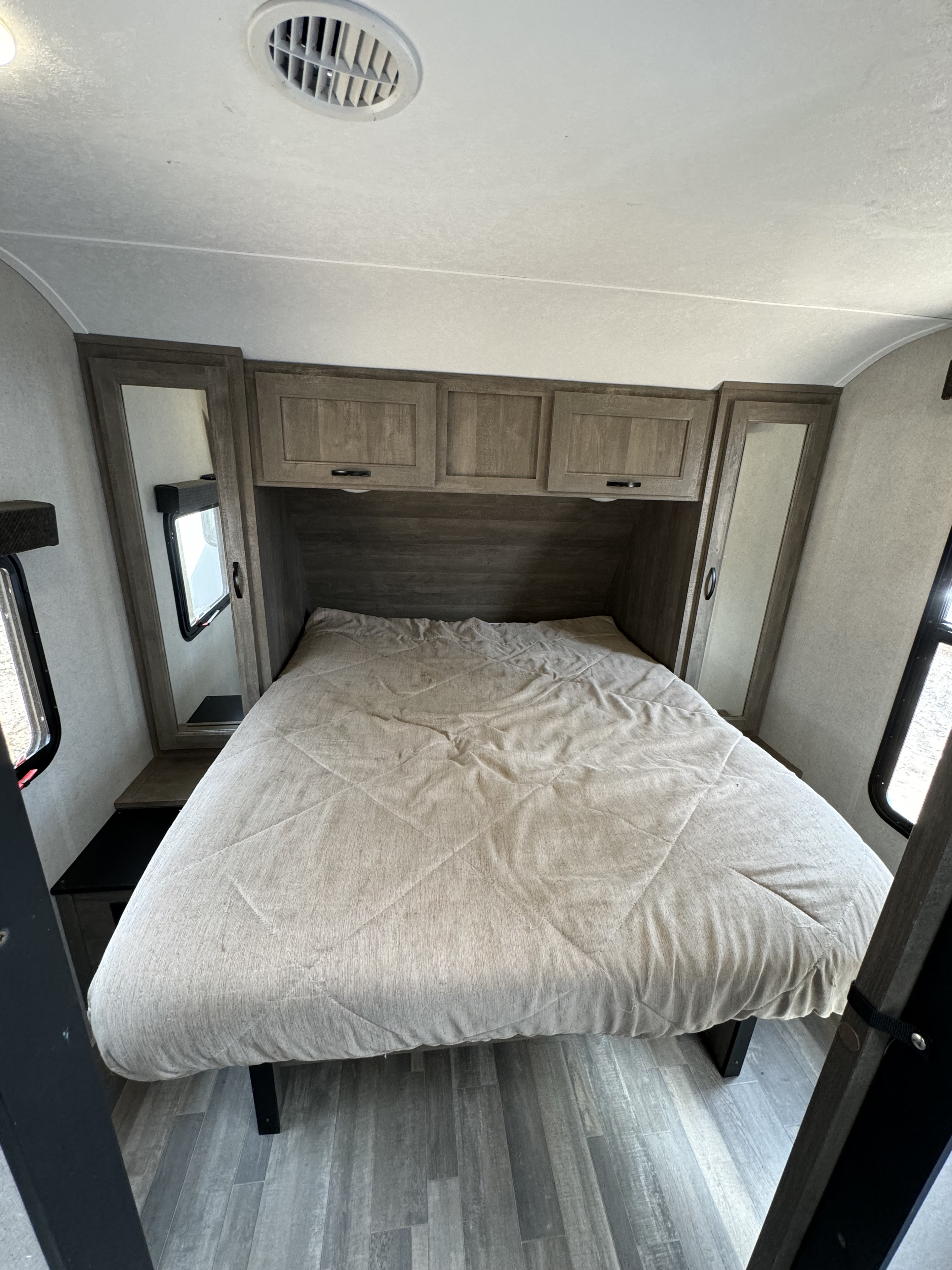 Comfortable RV rental bedroom with bed, overhead cabinets, mirrored wardrobes, windows, and AC vent for your travels.. Forest River Vibe 2021