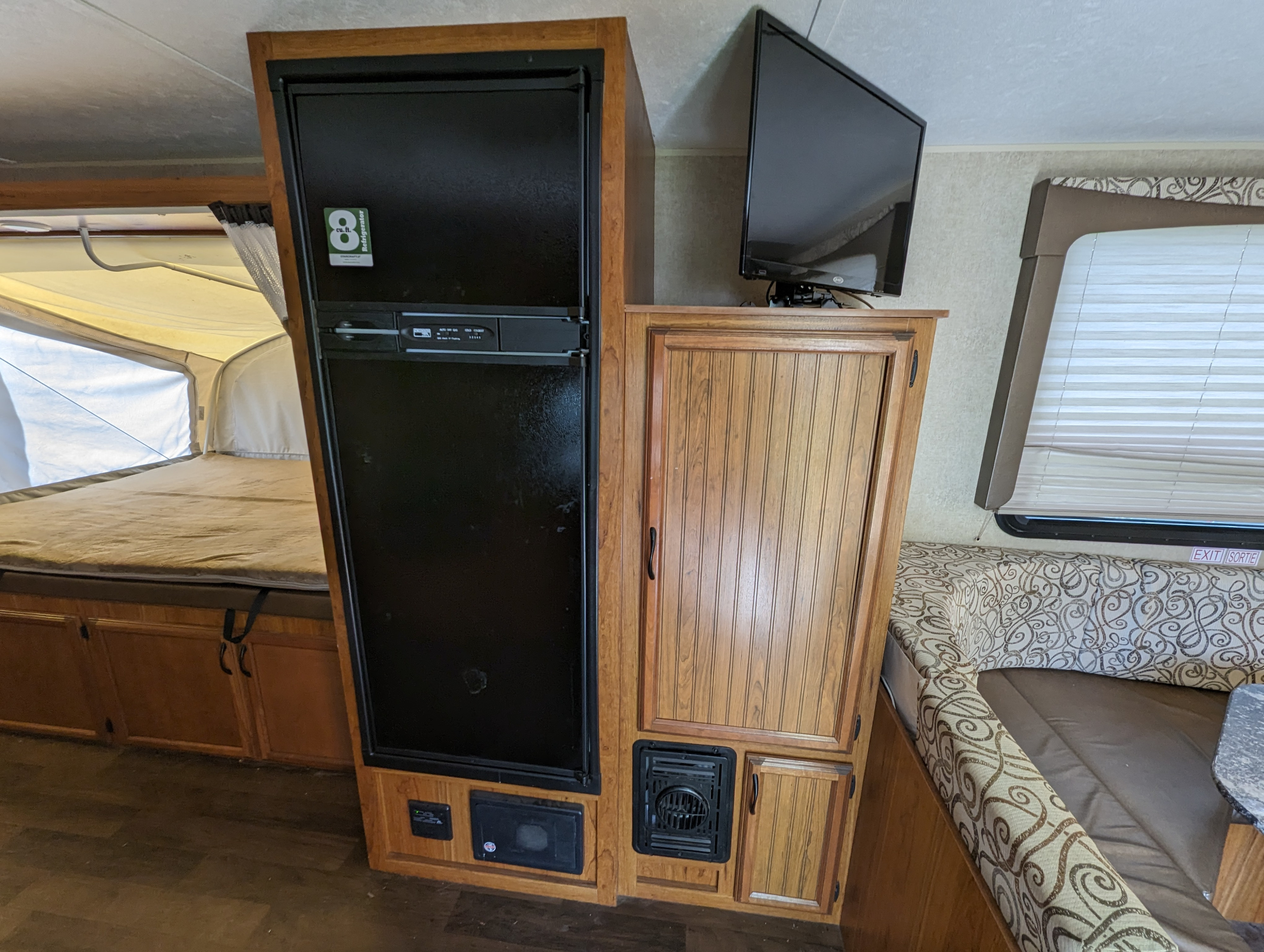 RV rental interior featuring a tall refrigerator, mounted TV, pop-out bed, and dinette seating with patterned cushions.. Starcraft Travel Star 2016
