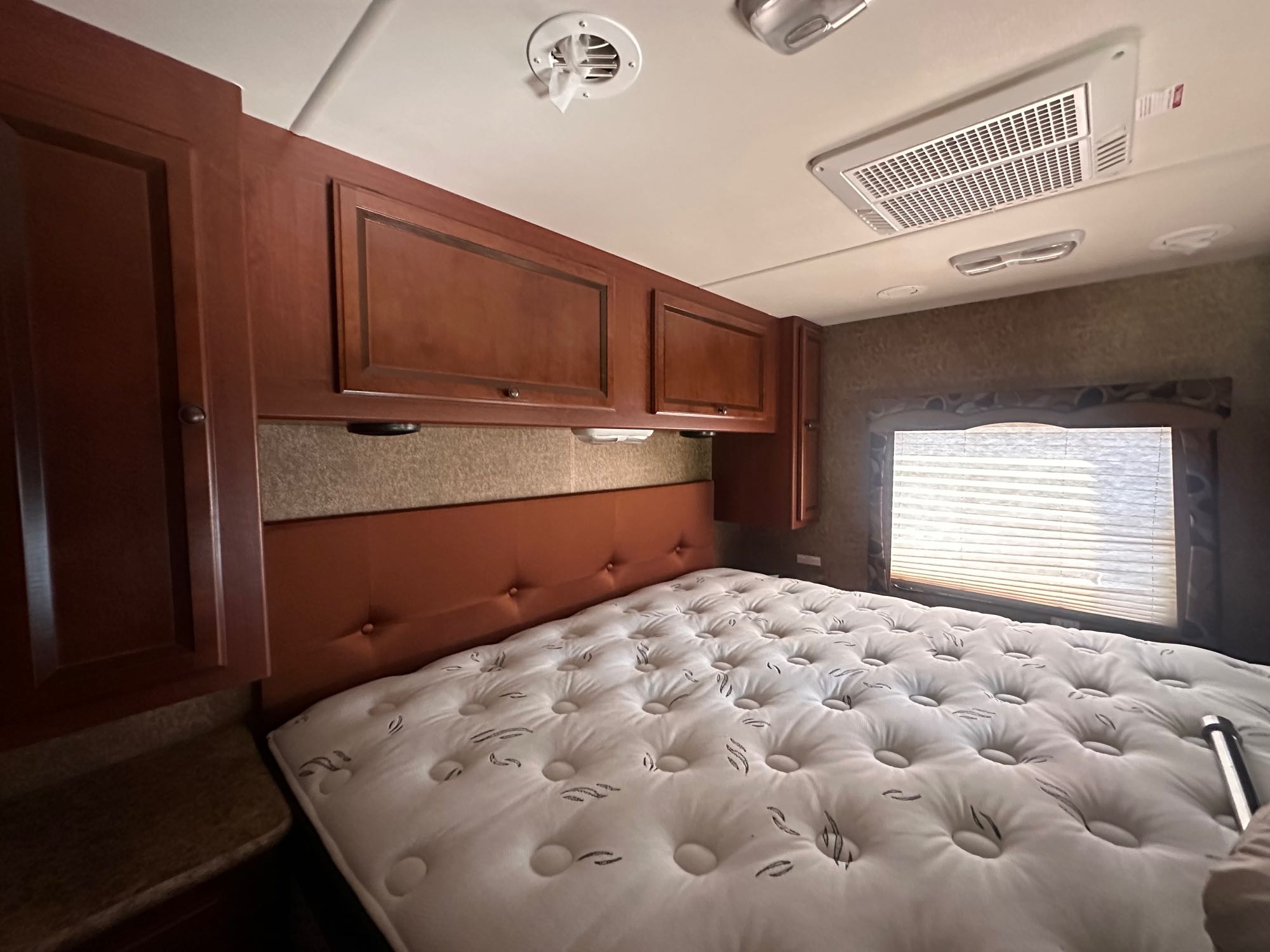 RV rental bedroom: A cozy space featuring a tufted mattress, overhead wood cabinets, and a sunlit window.. Thor Windsport 2014