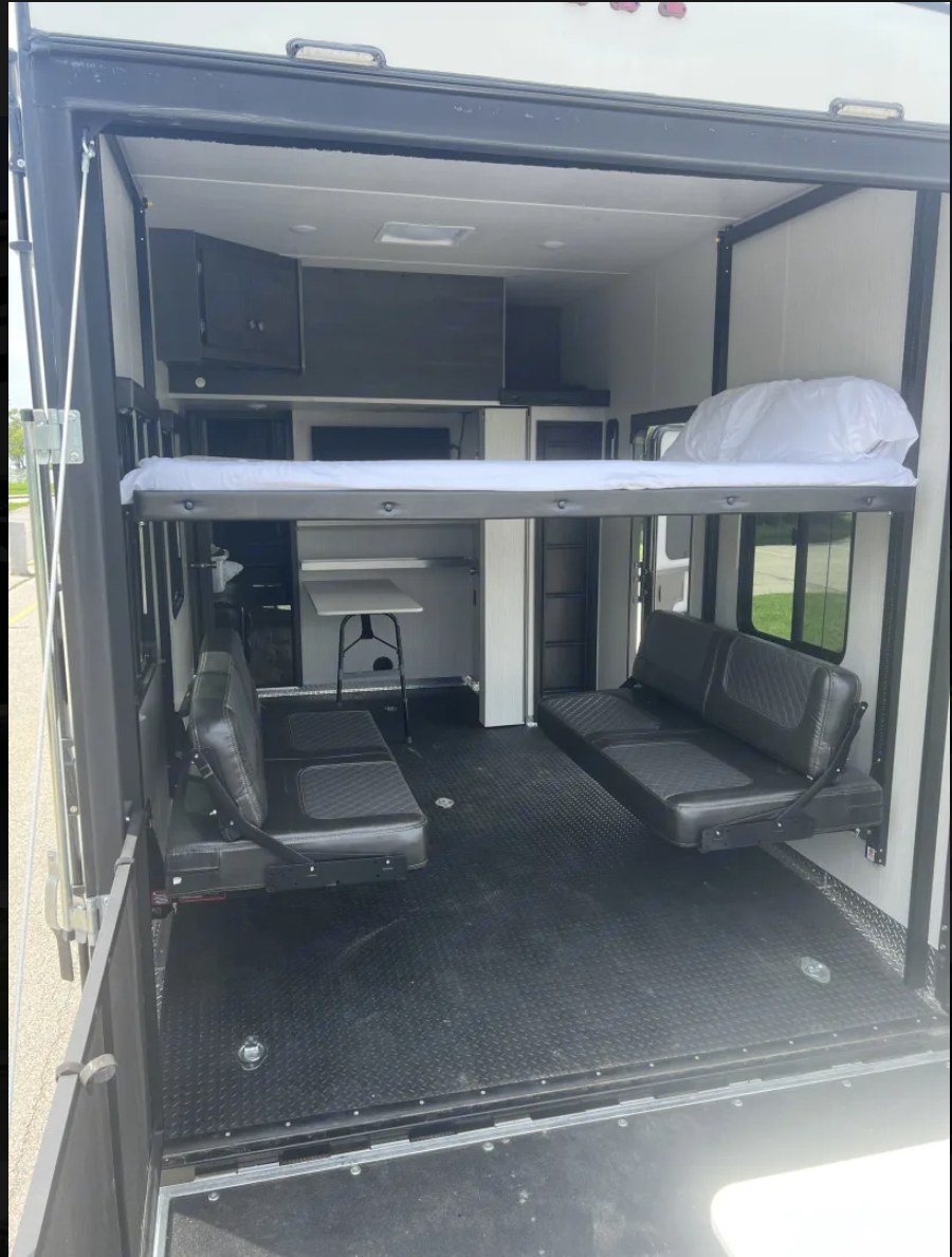 This RV rental toy hauler interior displays versatile space with an elevated bunk bed, two lower fold-down seats, and a rugged floor.. Heartland RVs Fuel Toy Hauler 2021