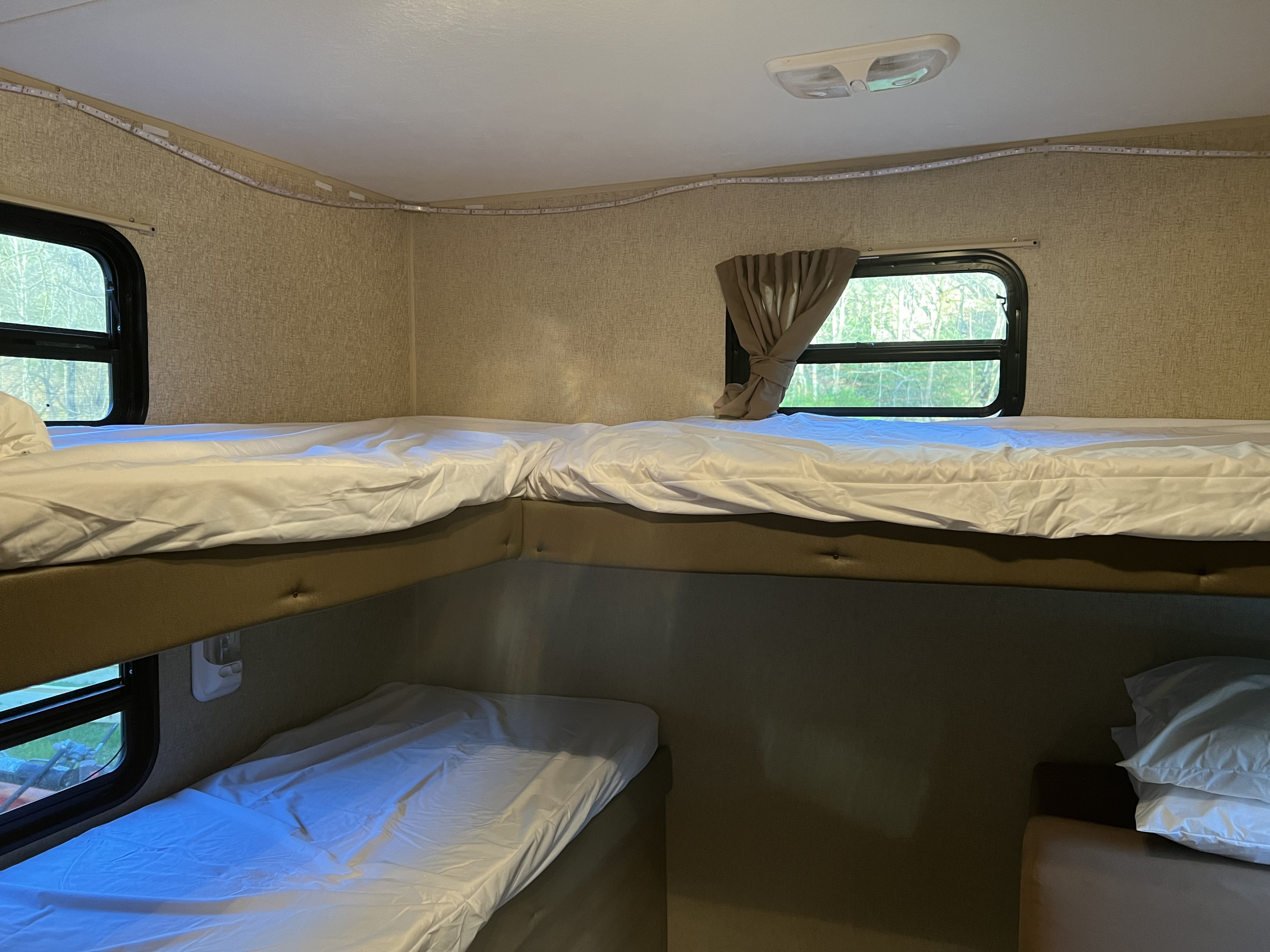 Inside an RV rental: a compact sleeping area with two upper bunks, a lower bunk, white bedding, and ambient LED lights.. Coachmen Catalina 293QBCK 2015