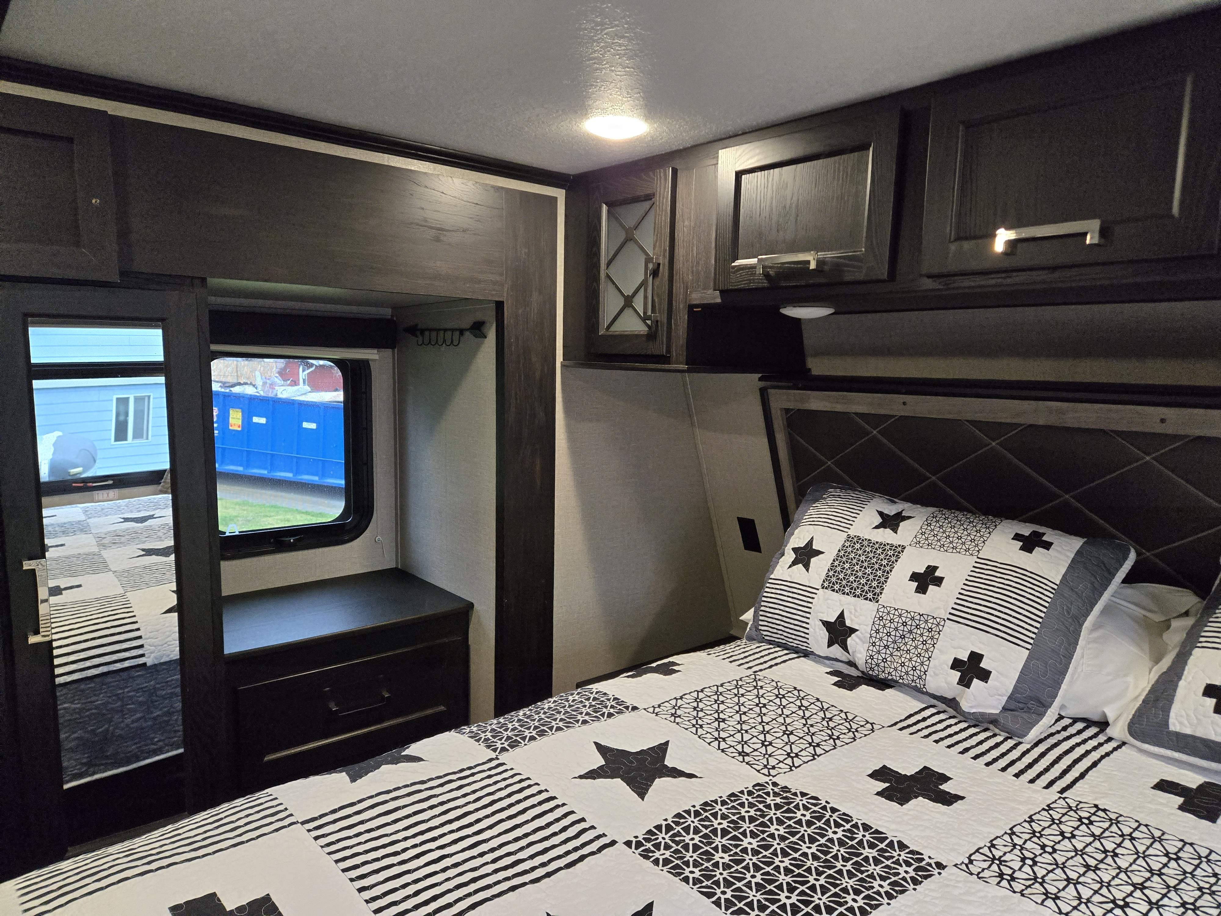 Cozy RV rental bedroom features a striking black and white geometric quilt, dark cabinetry, and a mirrored closet.. Keystone Fuzion 2018