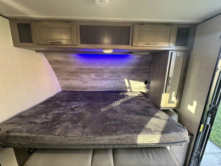 Experience a comfortable RV rental bedroom with a plush bed, overhead cabinets, blue lighting, and wardrobe storage.. Crossroads Sunset Trail Super Lite 2022
