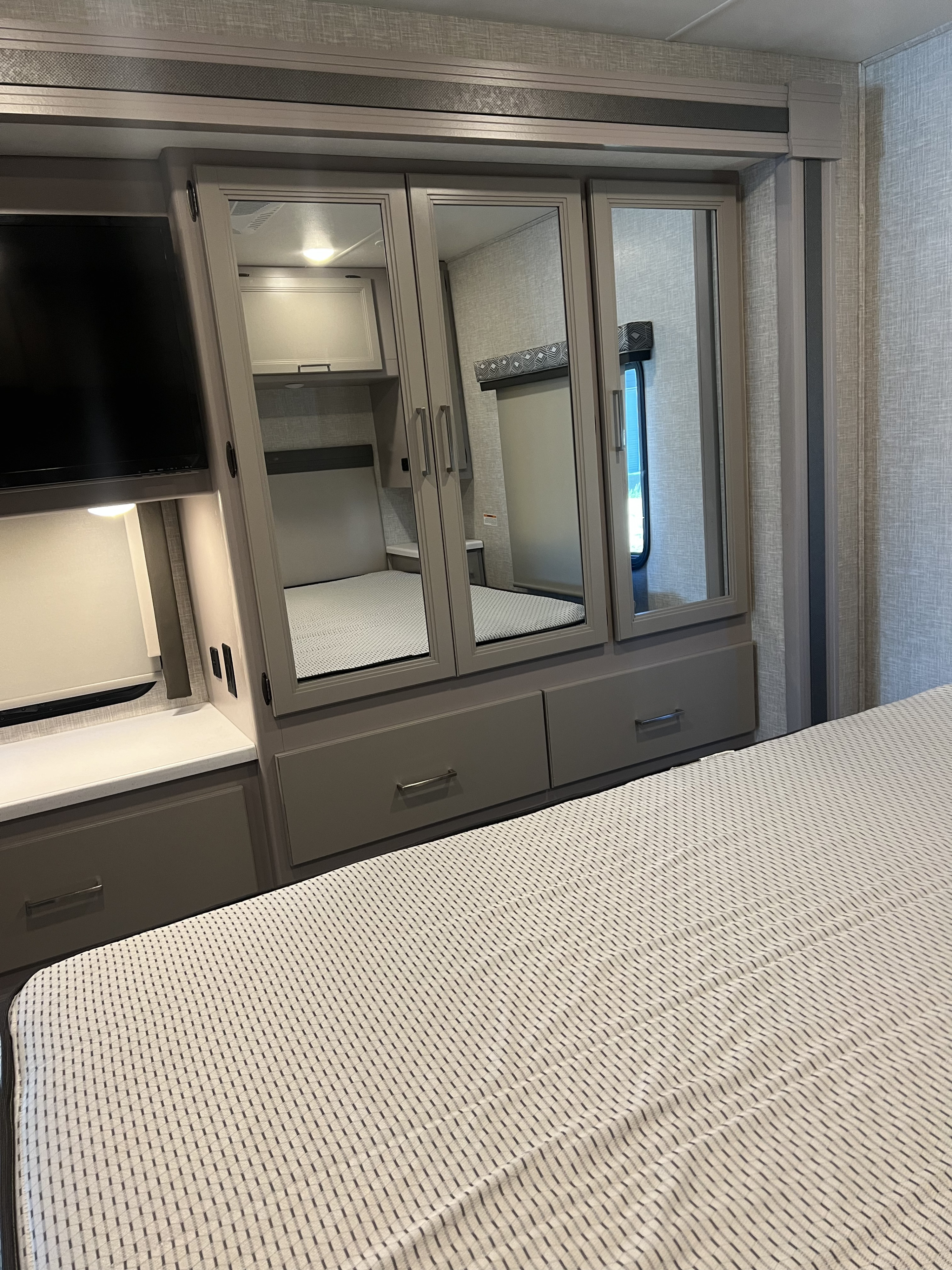 RV rental bedroom with patterned bed, mirrored wardrobe, TV, and storage drawers. A cozy, functional interior for your travels.. Thor Motor Coach Windsport 2022